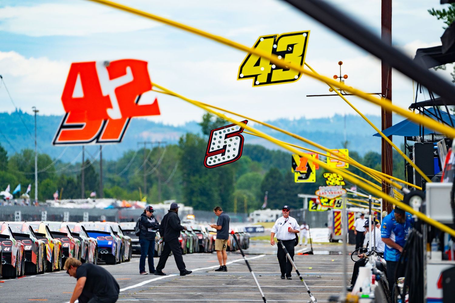 Race car being towed with crane truck against scenic mountain landscape background at racing event.