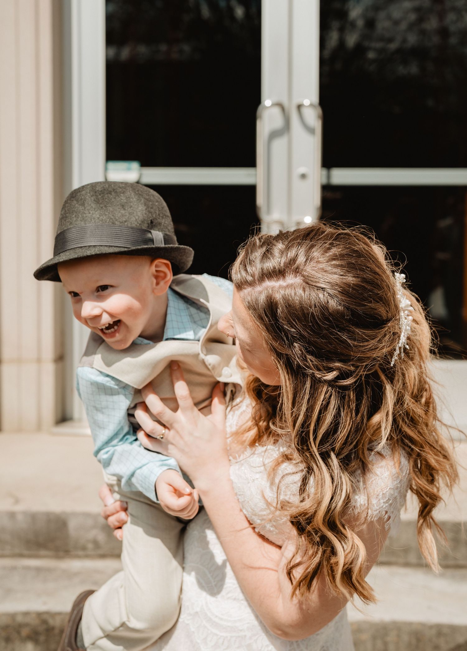 A joyful candid moment between a young child in a gray newsboy cap and someone in a light-colored dress outdoors.
