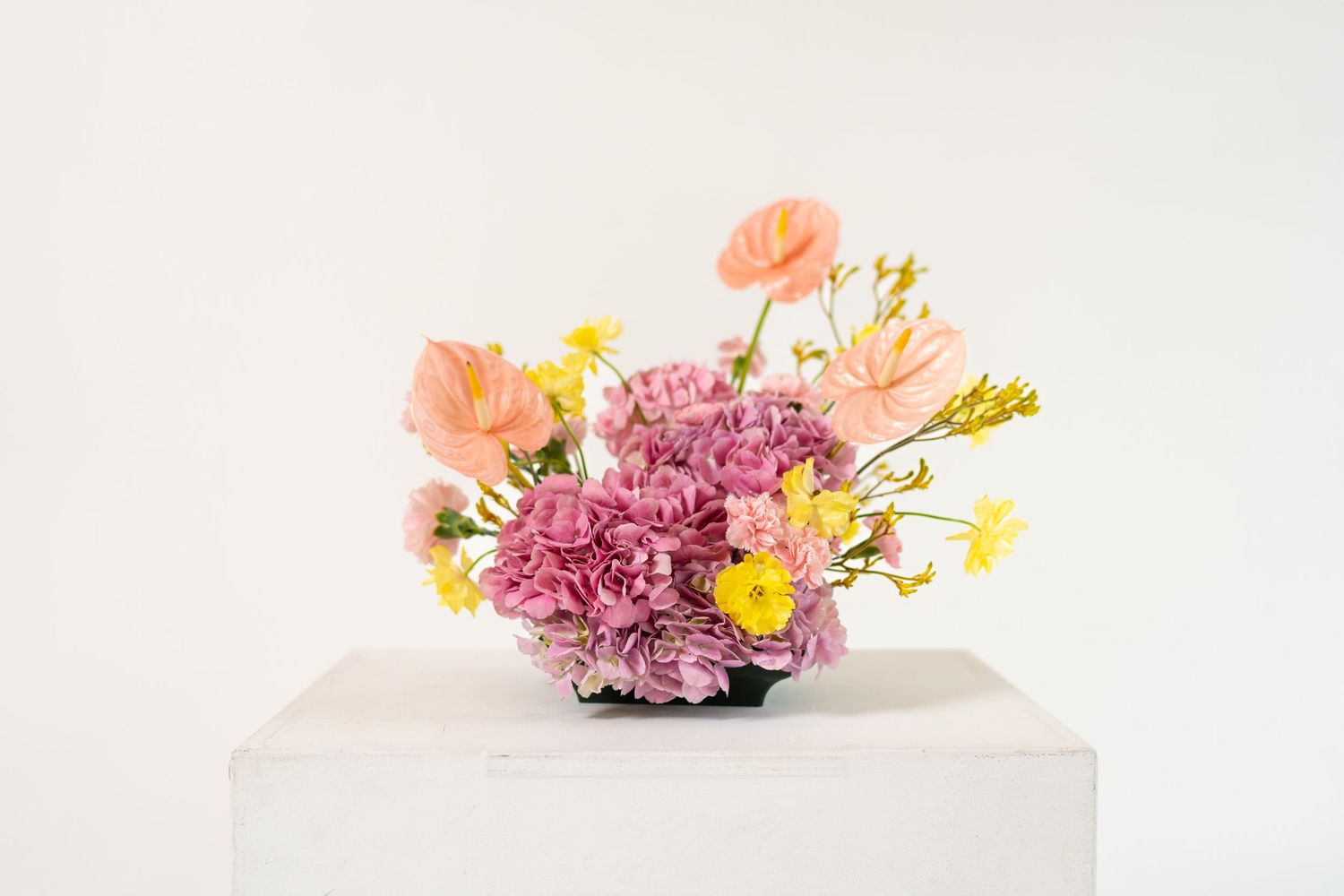 Vibrant floral arrangement with pink carnations and peach blooms displayed on white pedestal.
