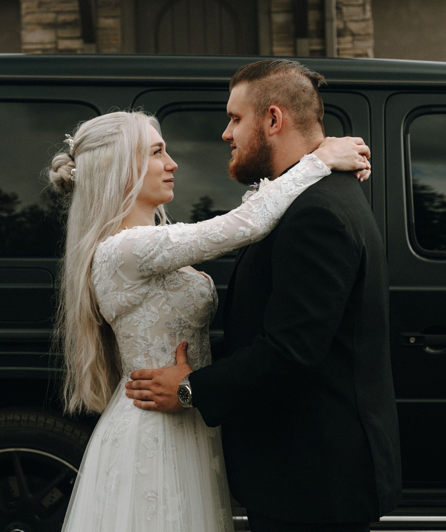 Couple in formal wedding attire sharing an intimate embrace beside a vintage car.