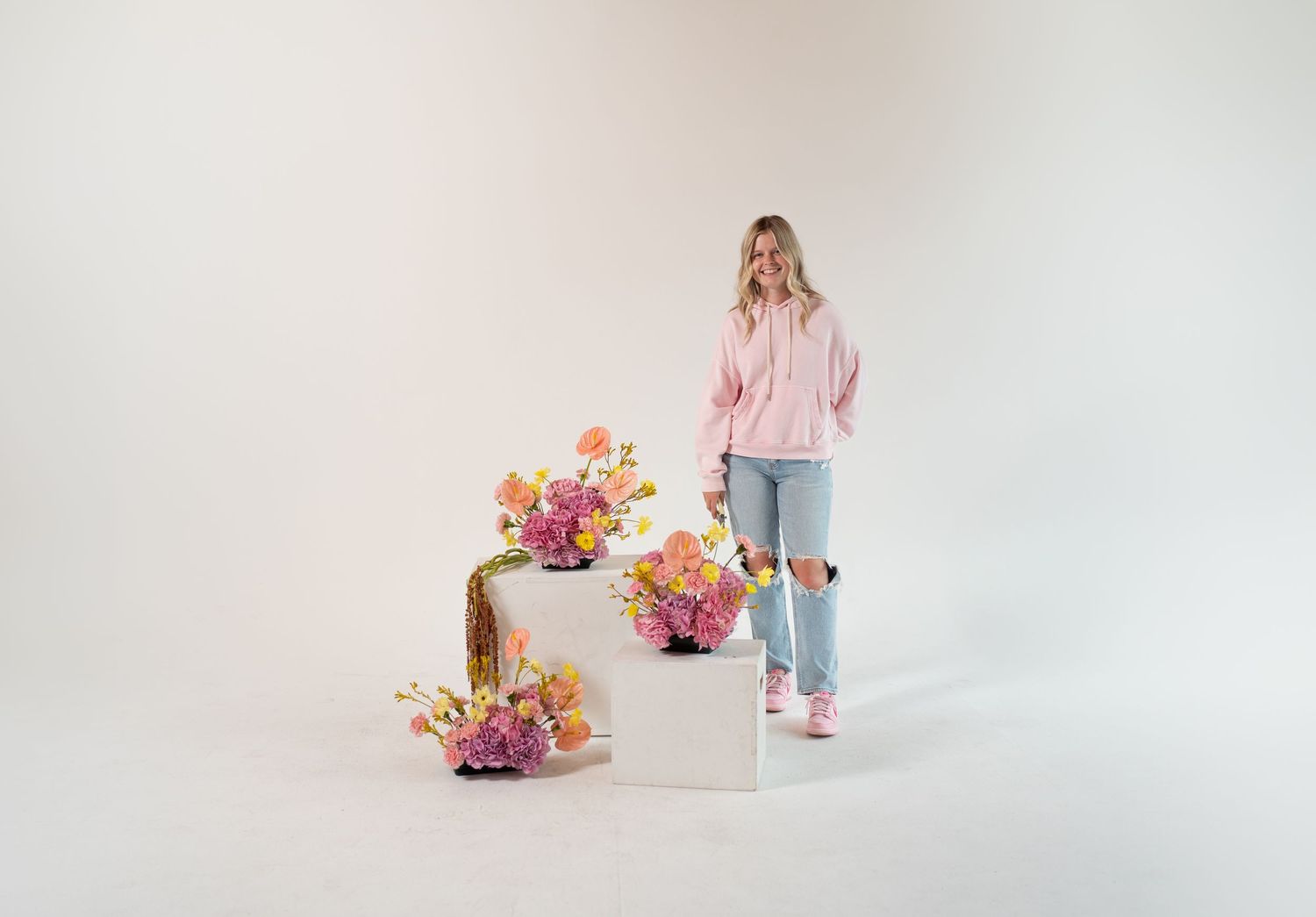 Casual spring fashion shoot with flowers arranged on white geometric platforms.