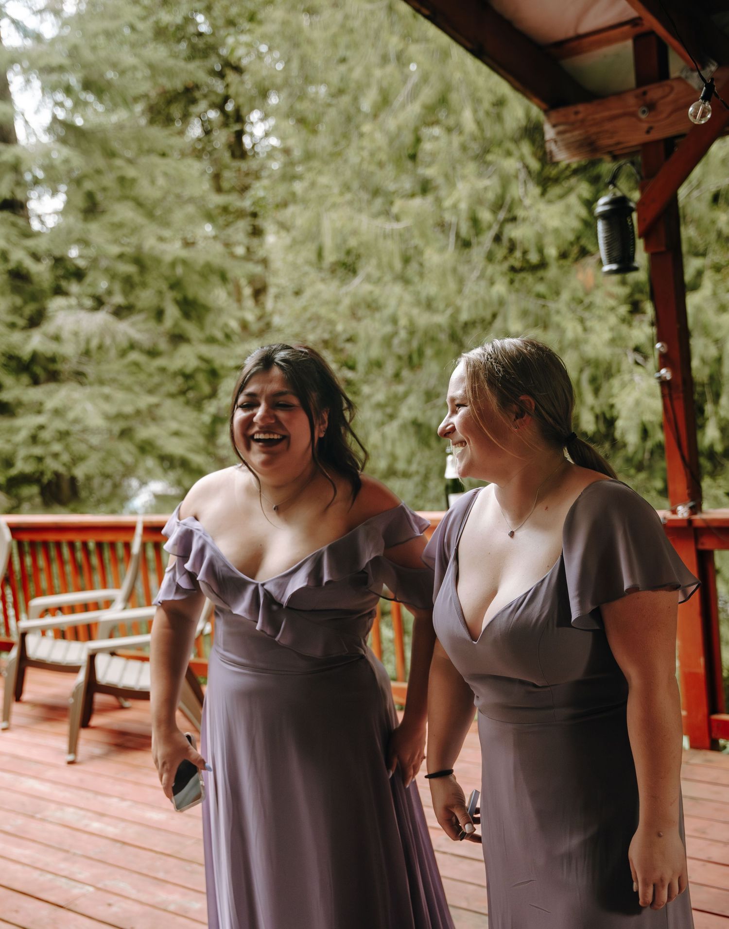 Bridesmaids in elegant grey dresses share a joyful moment on a wooden deck.
