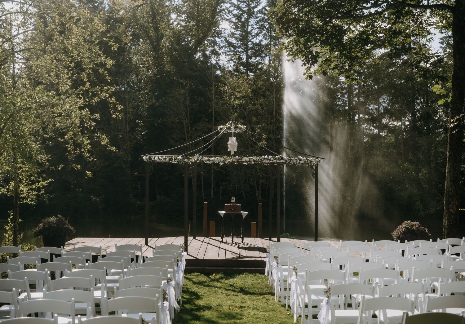 Rows of white chairs arranged for an outdoor wedding ceremony in a sunlit forest setting.