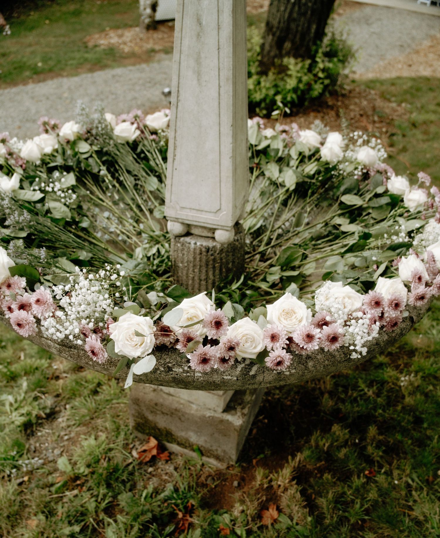 Pink and white roses arranged around a white pillar base with baby's breath accents.