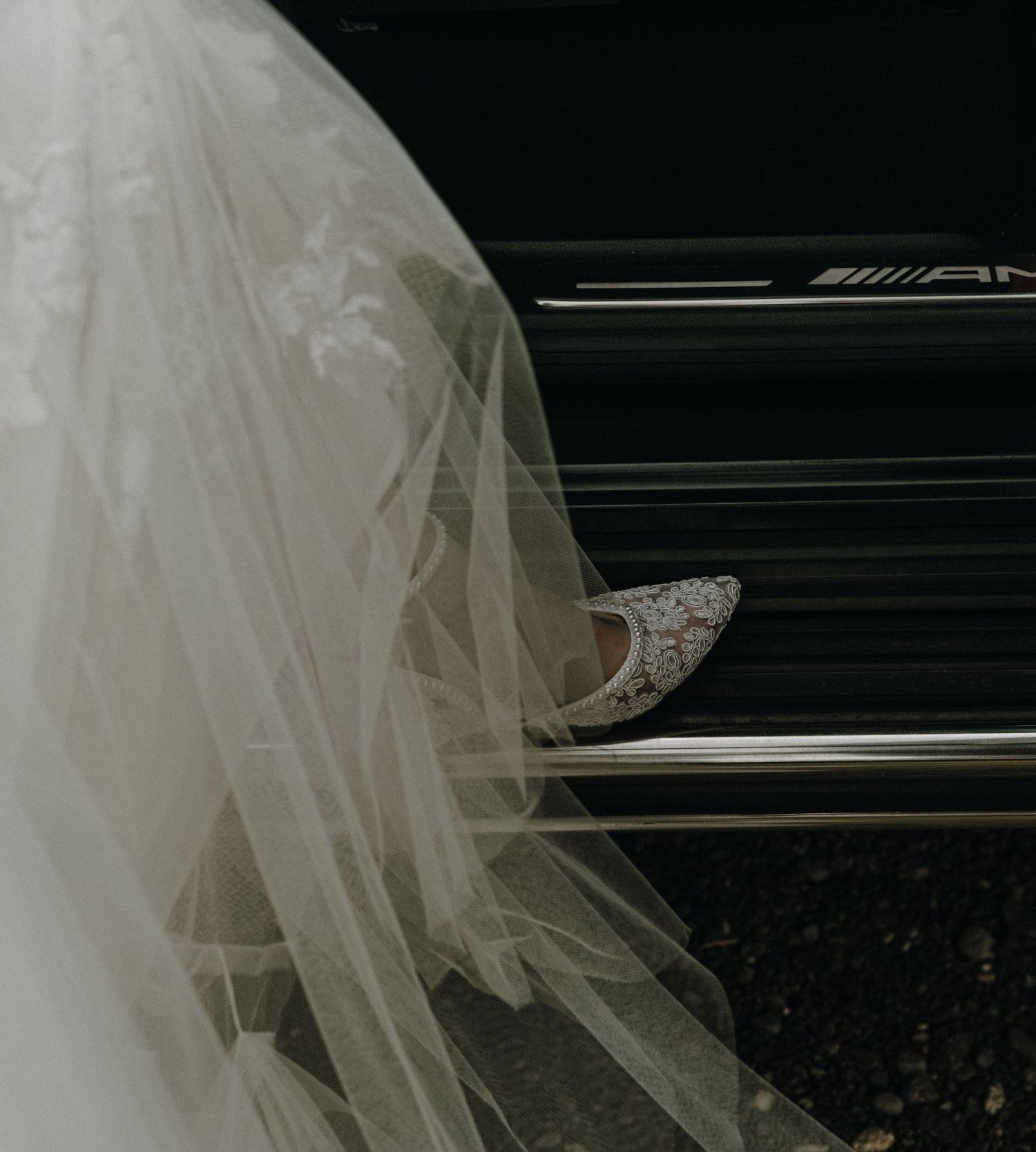 Close up detail of white wedding dress and veil flowing over dark piano keys.