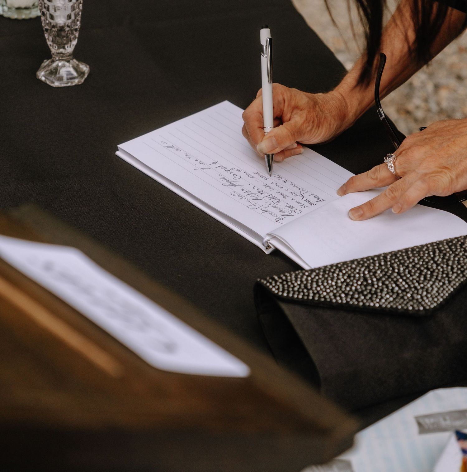 Close-up of hands signing wedding documents on dark wooden surface.