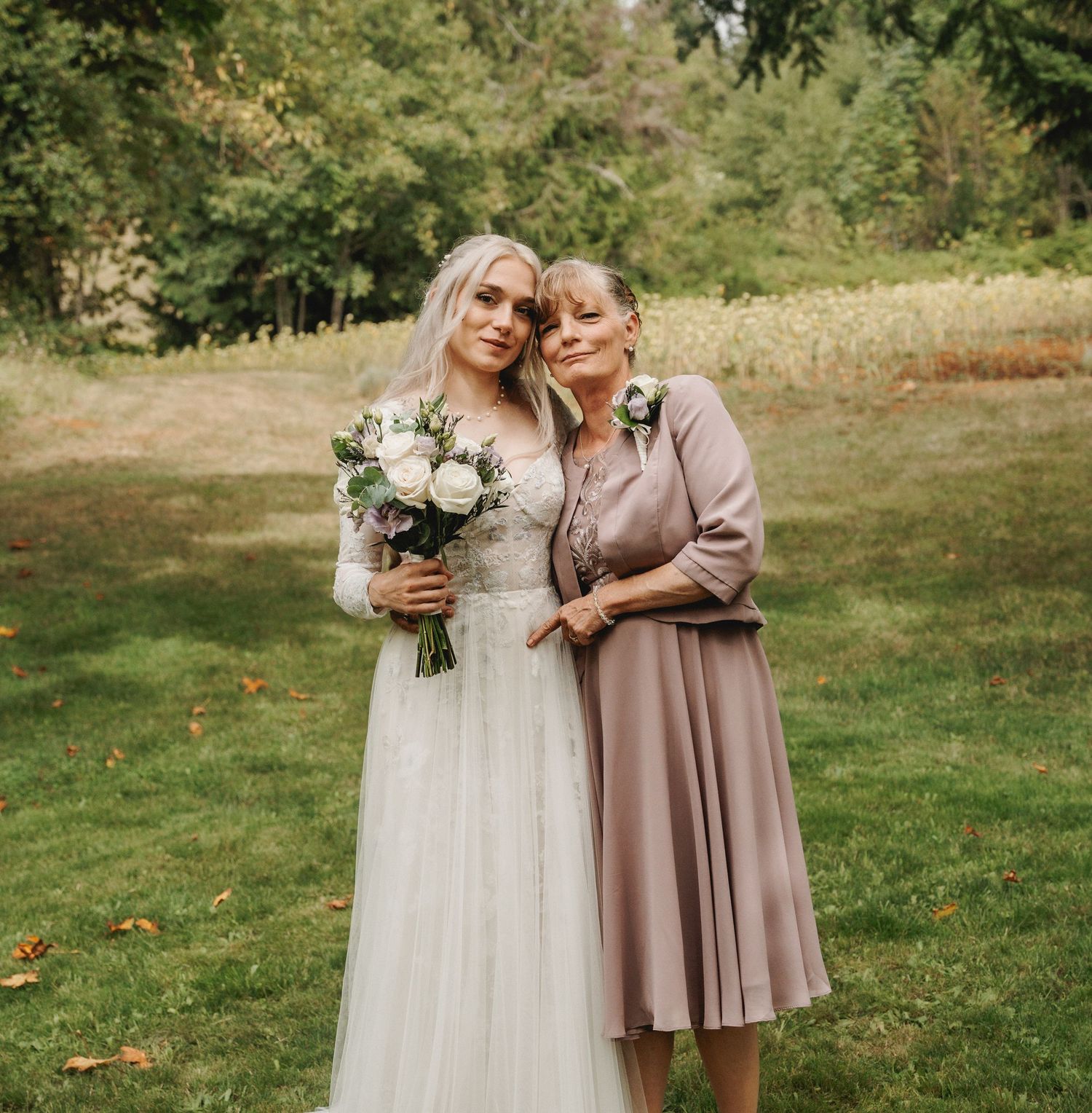 Wedding party poses on a grassy hillside wearing mauve and neutral-toned dresses.