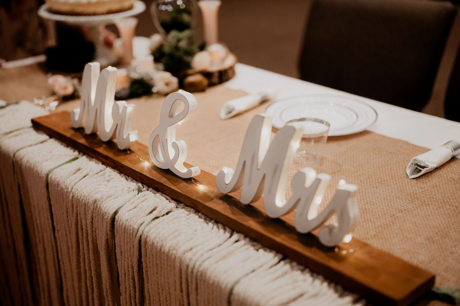 A rustic wooden Mr and Mrs wedding table sign displayed on a burlap-covered head table at a reception.