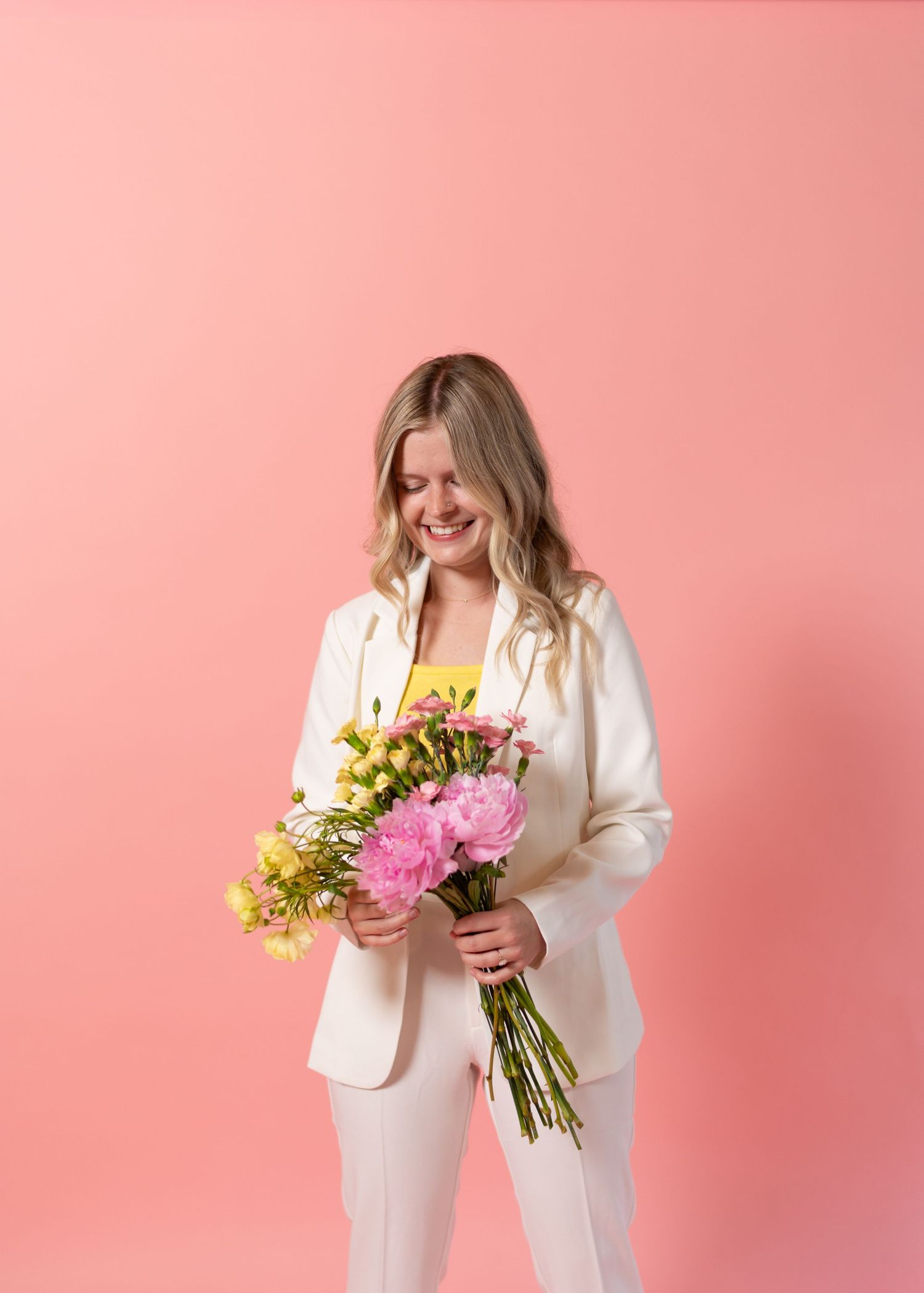 Person in white blazer holding spring flower bouquet against pink backdrop.