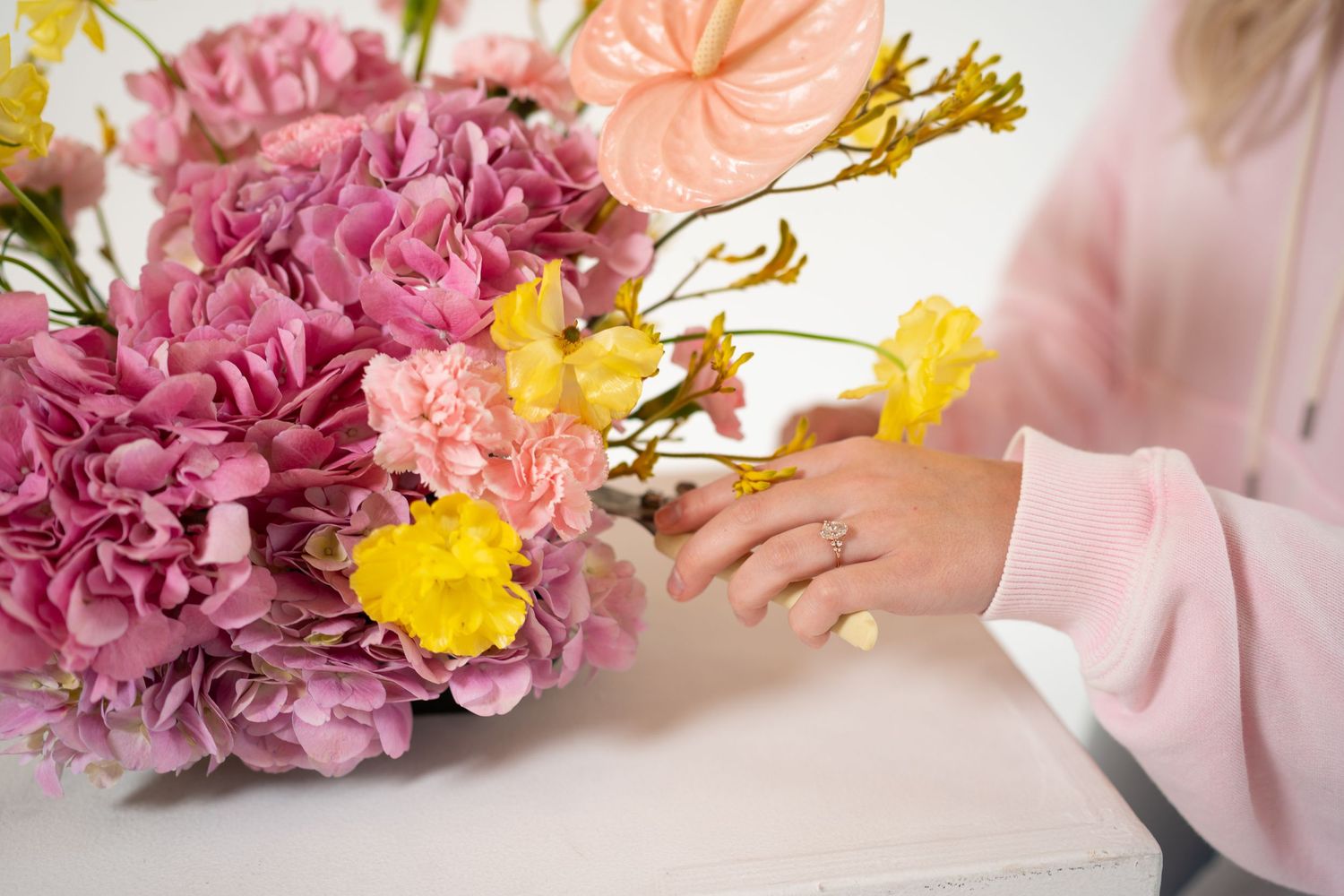 Detailed view of pink carnations and yellow flowers being styled on white surface.