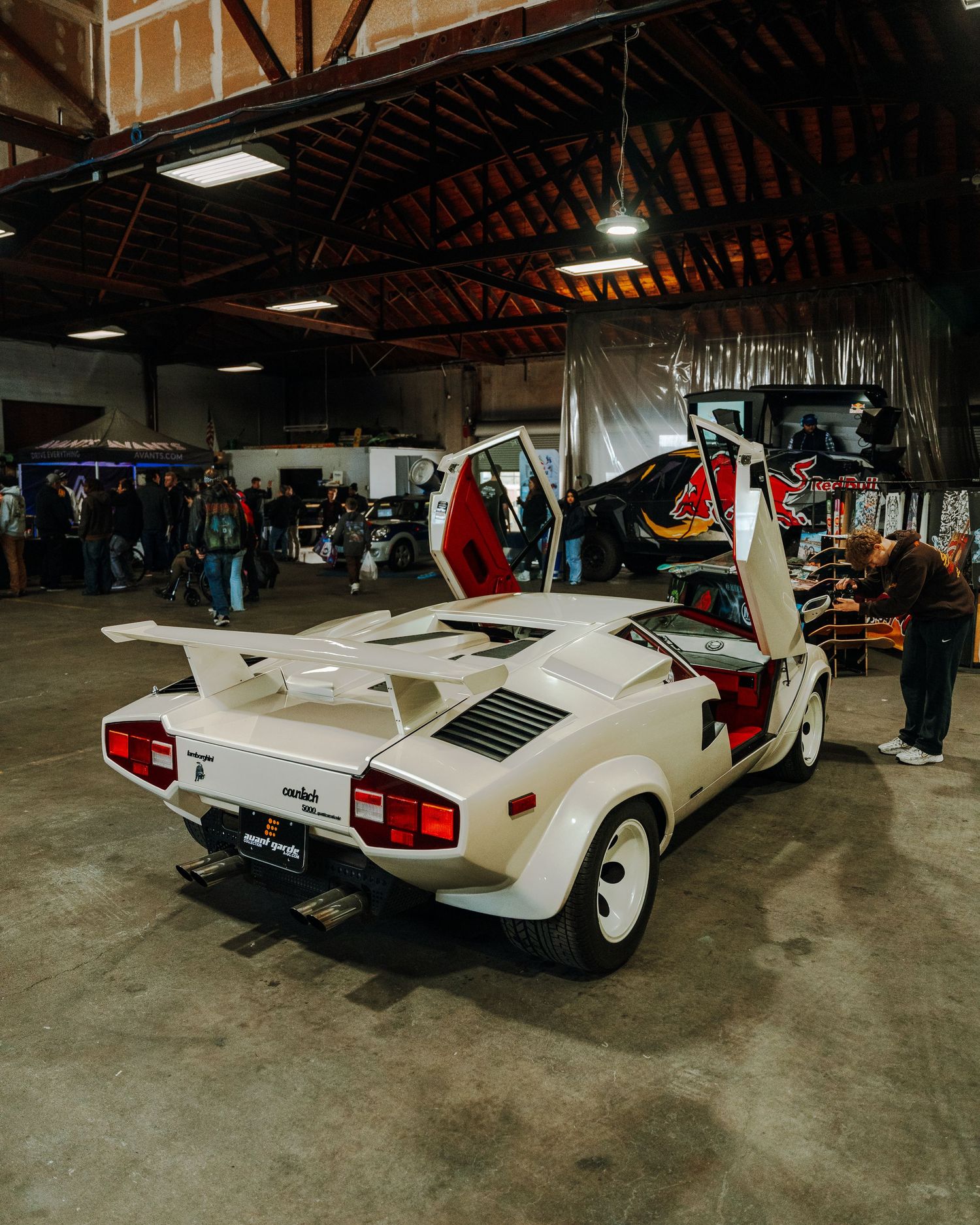 A white vintage Lamborghini Countach with scissor doors open is displayed inside a warehouse setting.