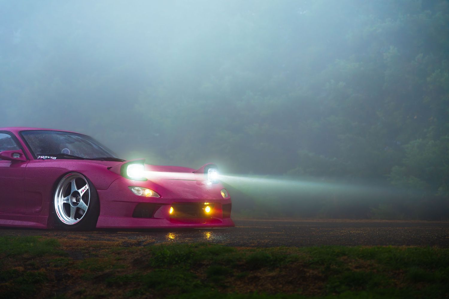 A purple sports car emerges dramatically through misty fog with glowing headlights and taillights.