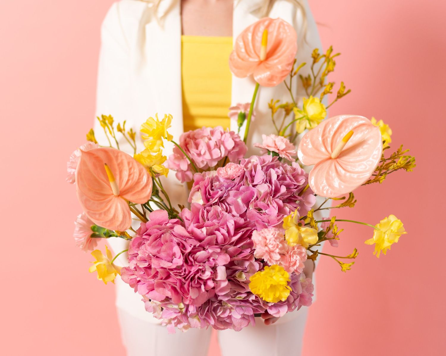 Colorful flower arrangement with pink and yellow blooms against a coral pink background.