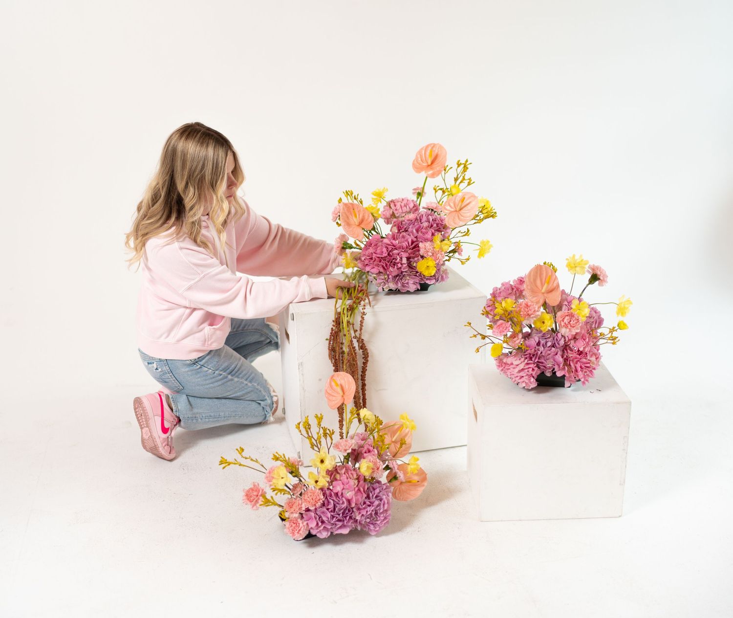 Floral designer arranging colorful spring bouquets on white display platforms.