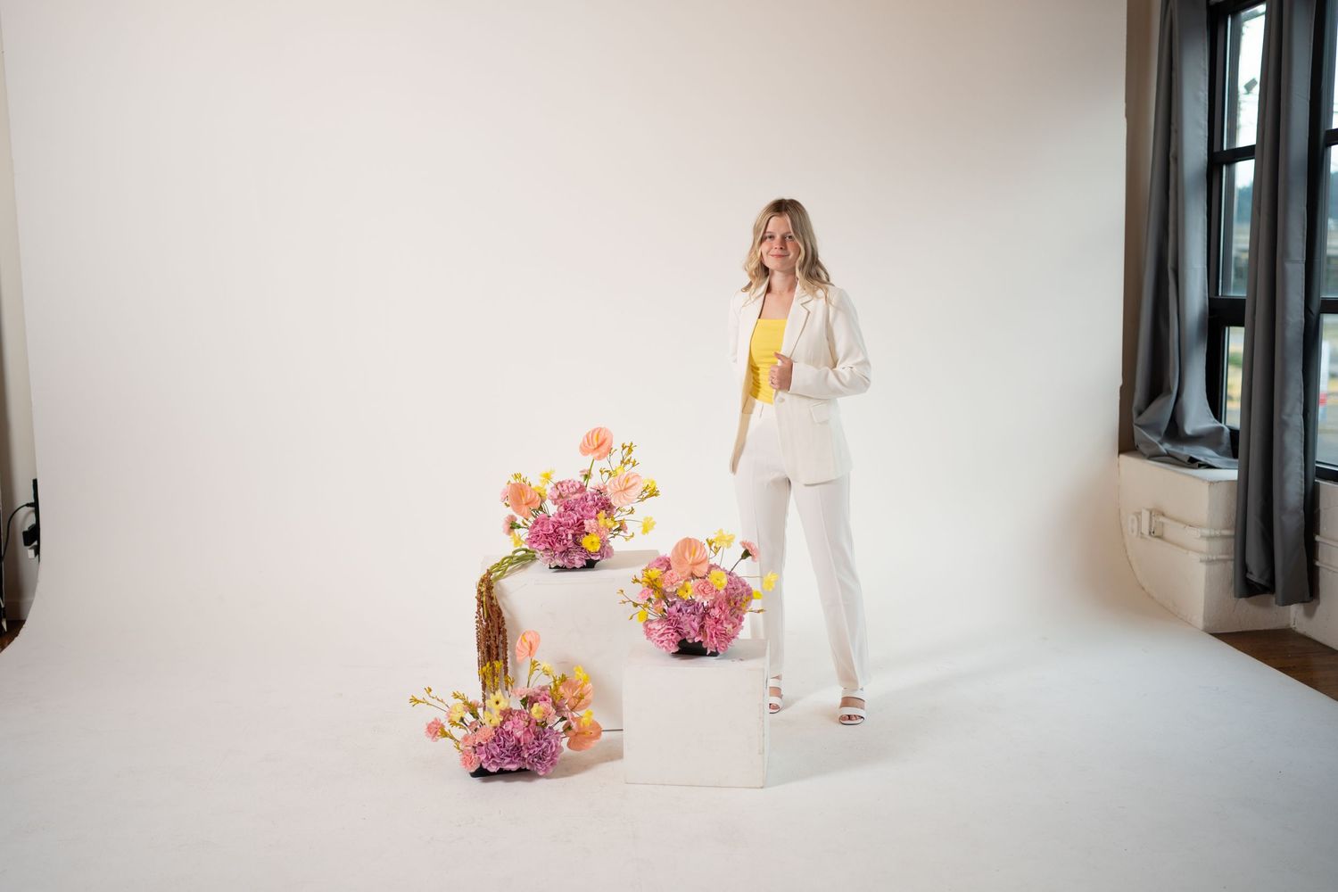 Fashion photo of a white pantsuit styled with yellow accents and floral arrangements on wooden blocks.