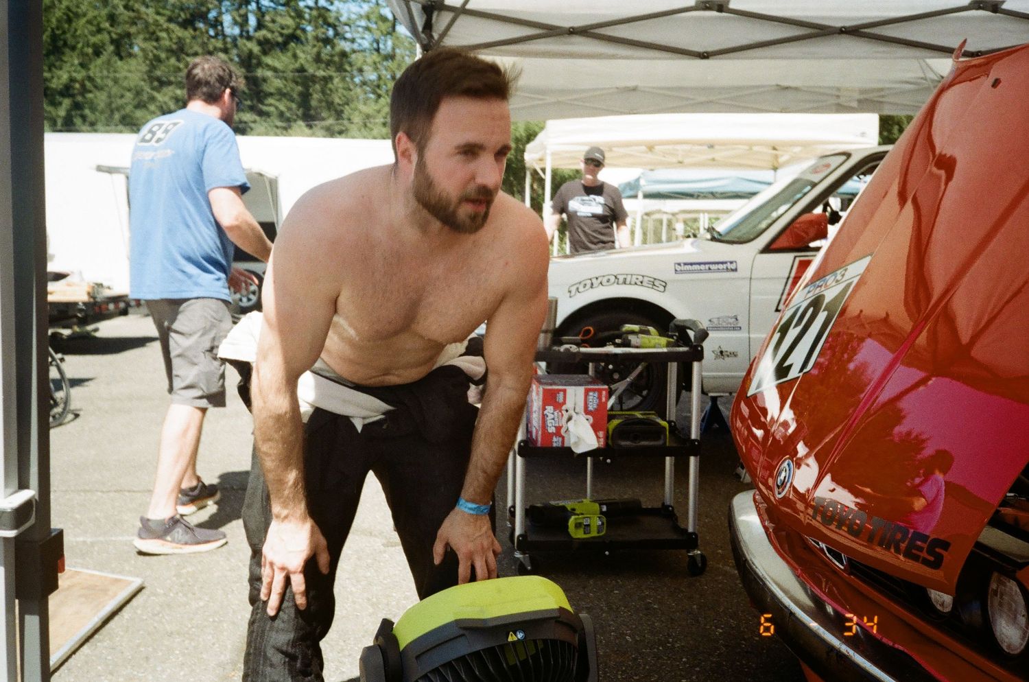 Shirtless athletes perform rigorous CrossFit workouts at an outdoor competition under white tents.