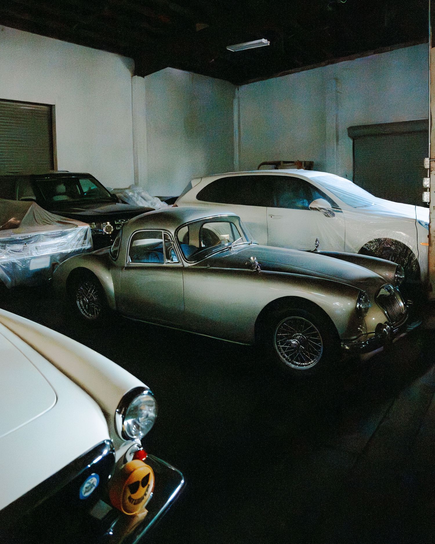 Classic cars including a vintage MG and other luxury vehicles lined up in a dimly lit garage or showroom space.