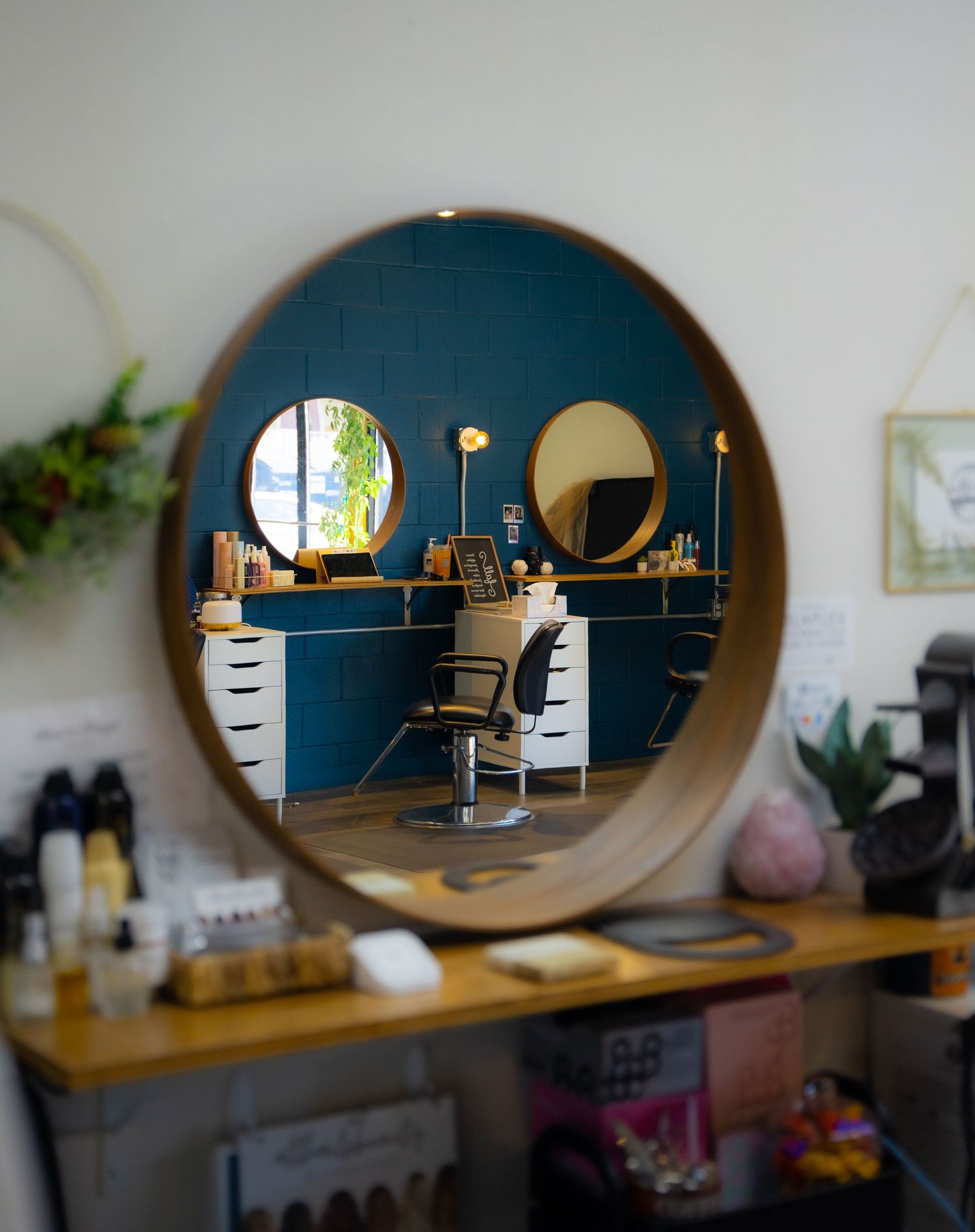 Hair salon workstation with round mirror, blue accent wall and indoor plants.