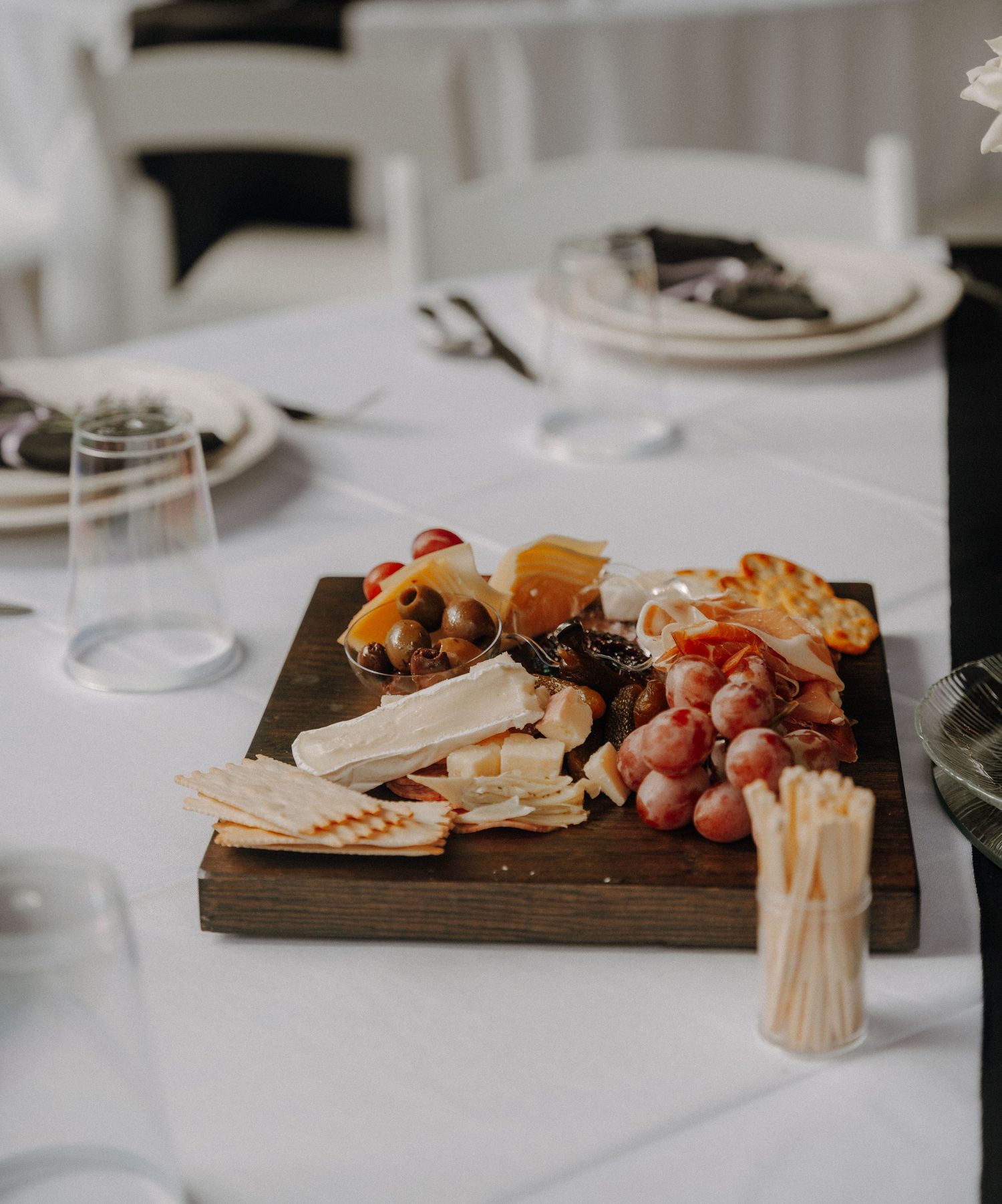 Elegant charcuterie and cheese board display on white tablecloth at reception.