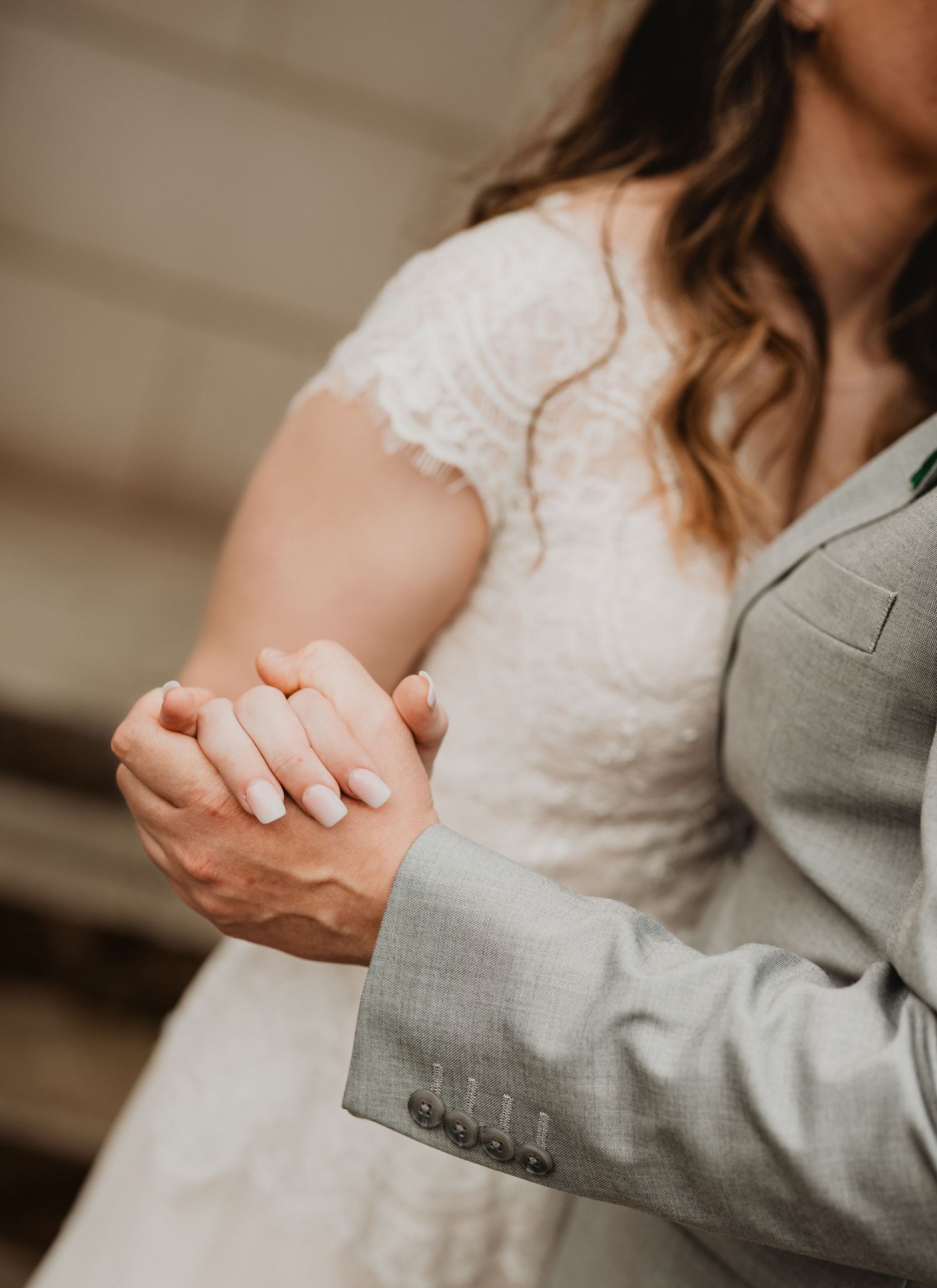 A close up sequence of two people holding hands in wedding attire, showing gray suit and white lace dress details.