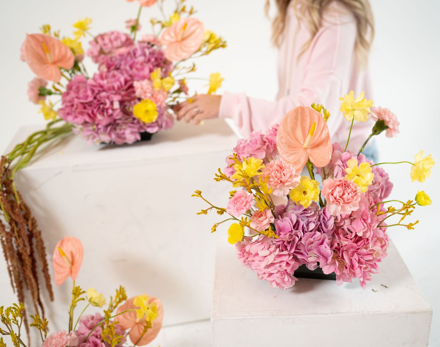 Fresh pink carnations and yellow flowers arranged in elegant glass vases on a white surface.