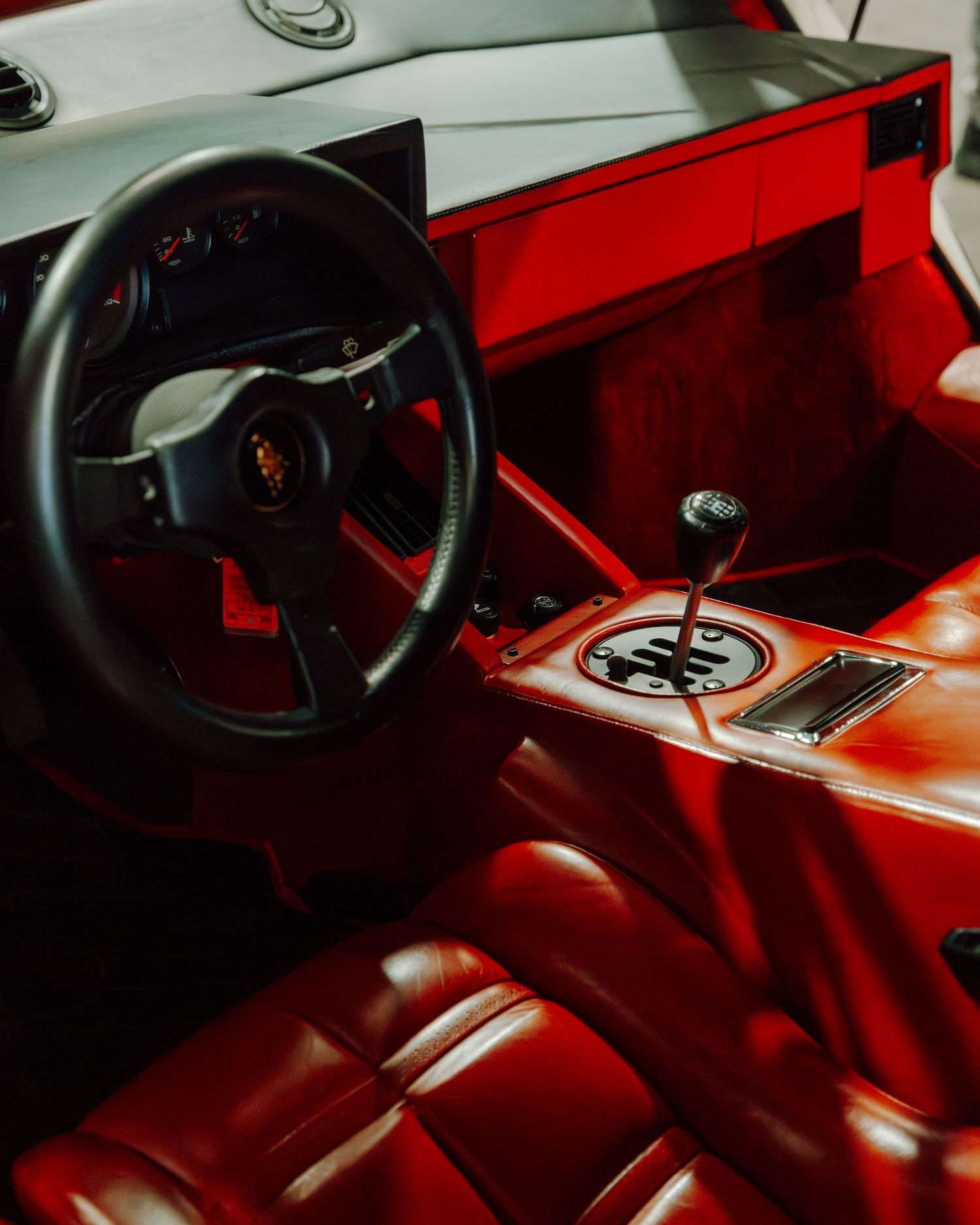 Interior view of a luxury sports car with red leather seats and dashboard, showing a black steering wheel and manual gearshift.