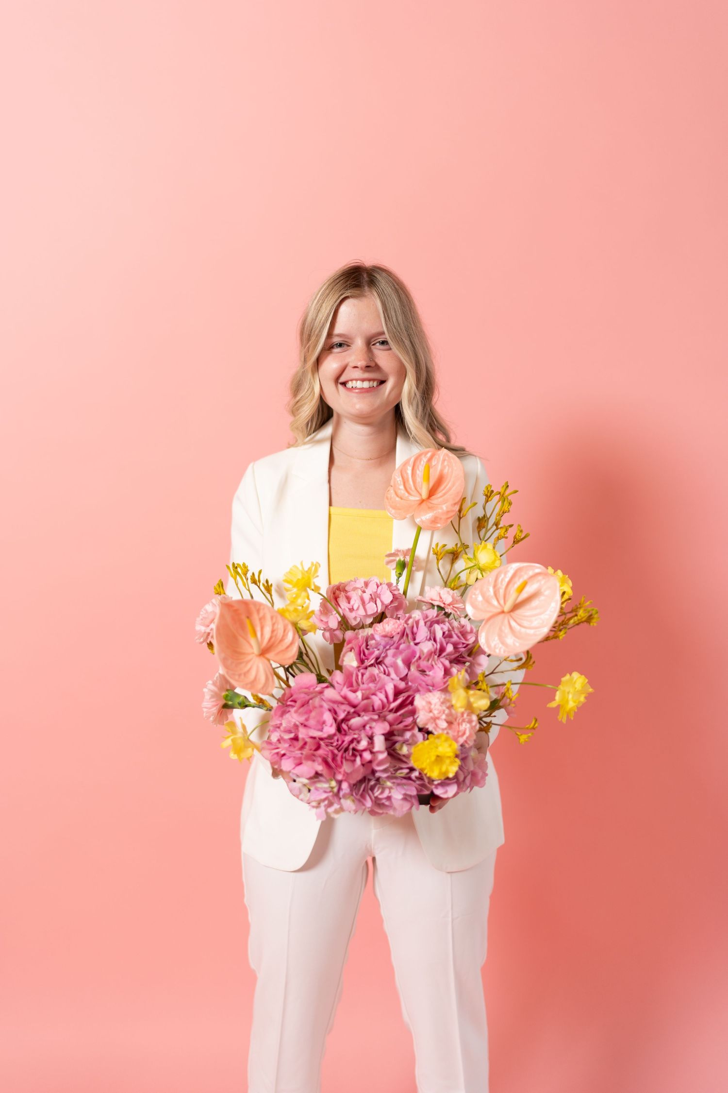 Floral arrangement showing vibrant pink and yellow flowers held against a coral pink backdrop.