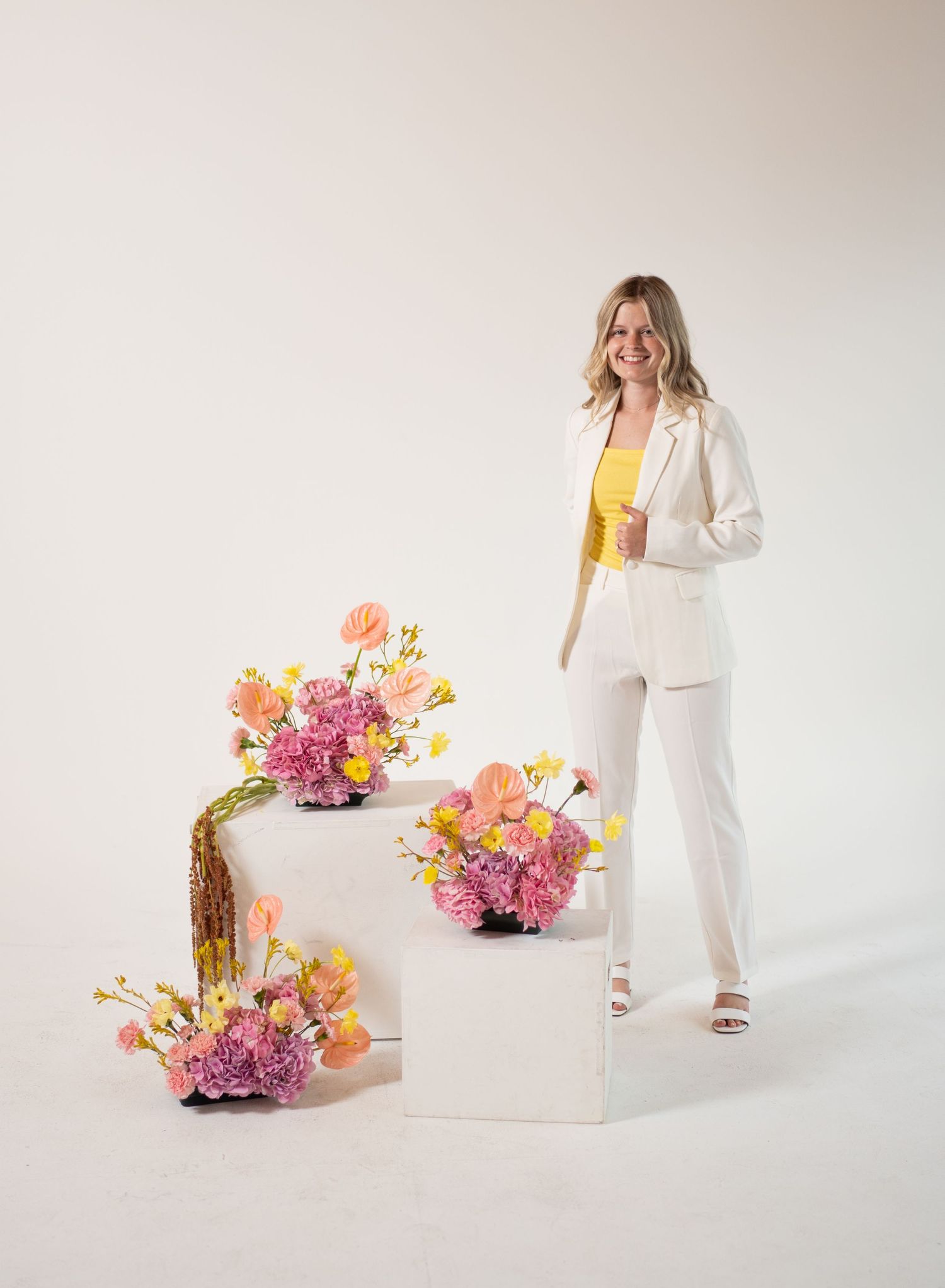 Lifestyle photo shoot with flowers and person in white outfit against neutral background.
