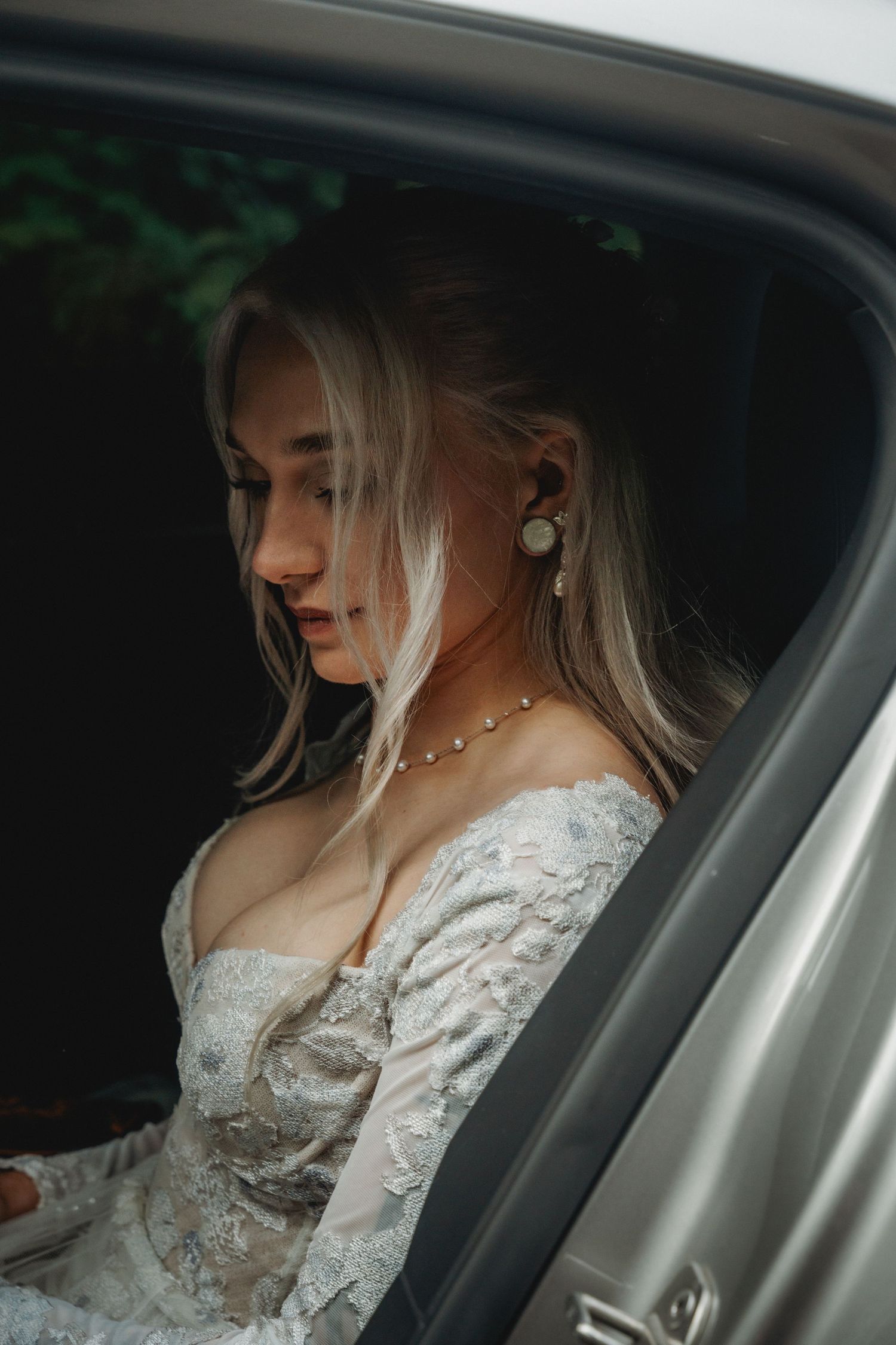 A woman in a white lace wedding dress sits in an elegantly posed car portrait sequence.