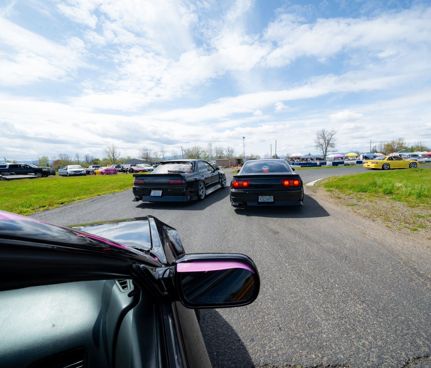 Panoramic view of multiple vehicles parked in a large gravel parking lot under cloudy skies.