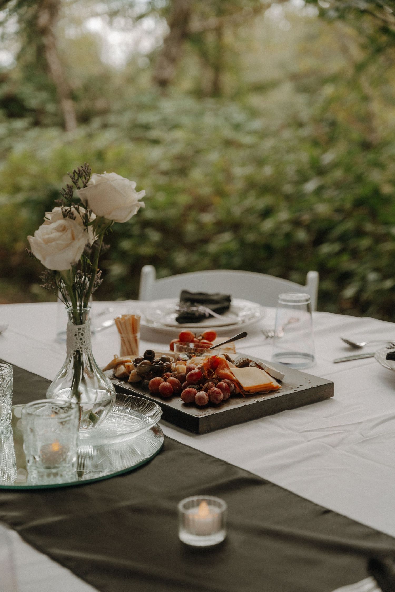 Elegant wedding reception table setting with roses, candles and appetizers on white tablecloth.