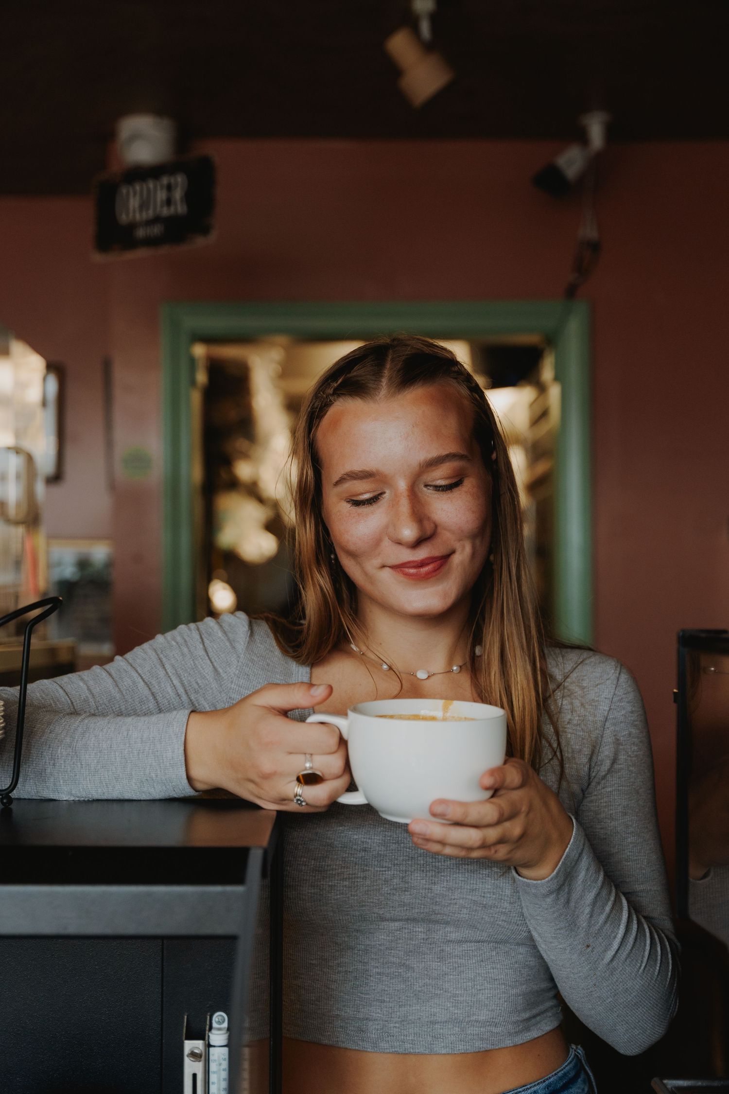 Person in grey sweater enjoying a warm beverage in cozy cafe setting.