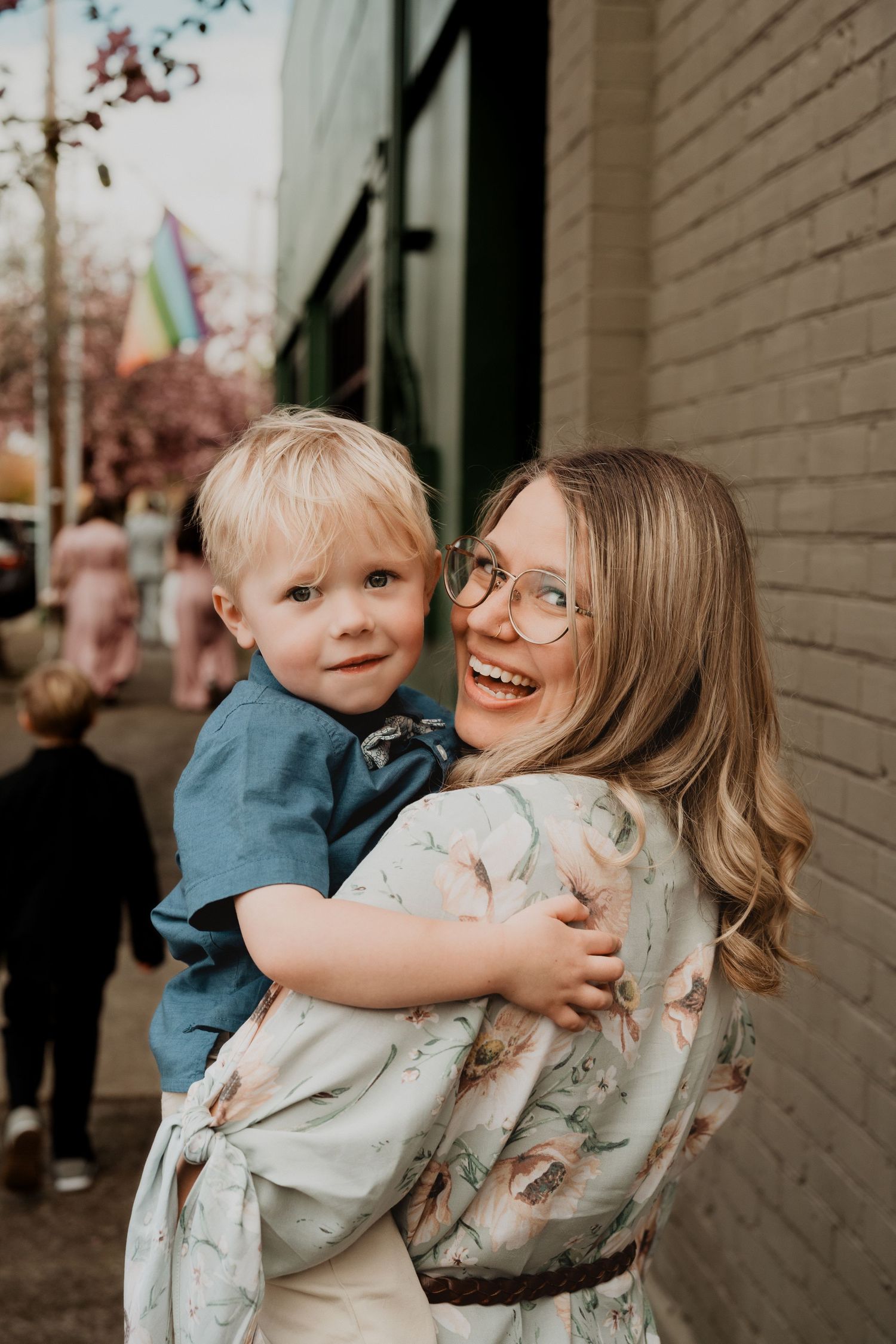 A sweet candid moment between parent and child standing against a brick wall on a sunny day.