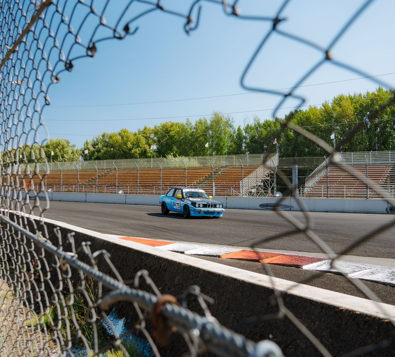 Multiple sequential images showing a racing car navigating a racetrack turn with motion blur and chainlink fencing.
