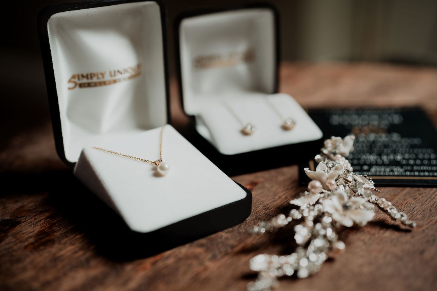 A collection of wedding rings and jewelry displayed in white velvet boxes against a dark wooden surface.