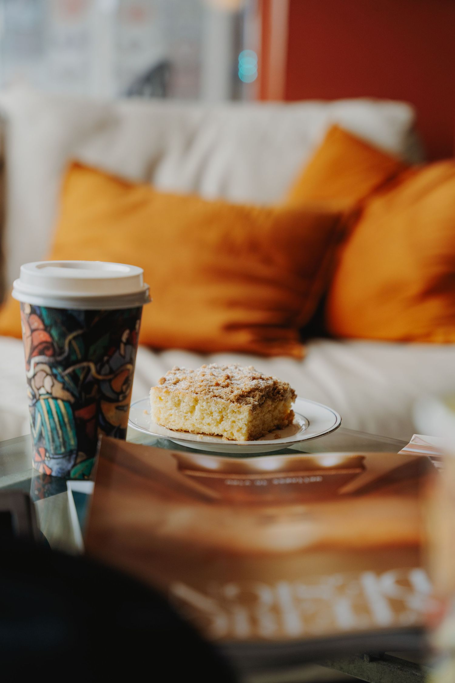 Coffee cup and pastry dessert on table with orange pillows in background.
