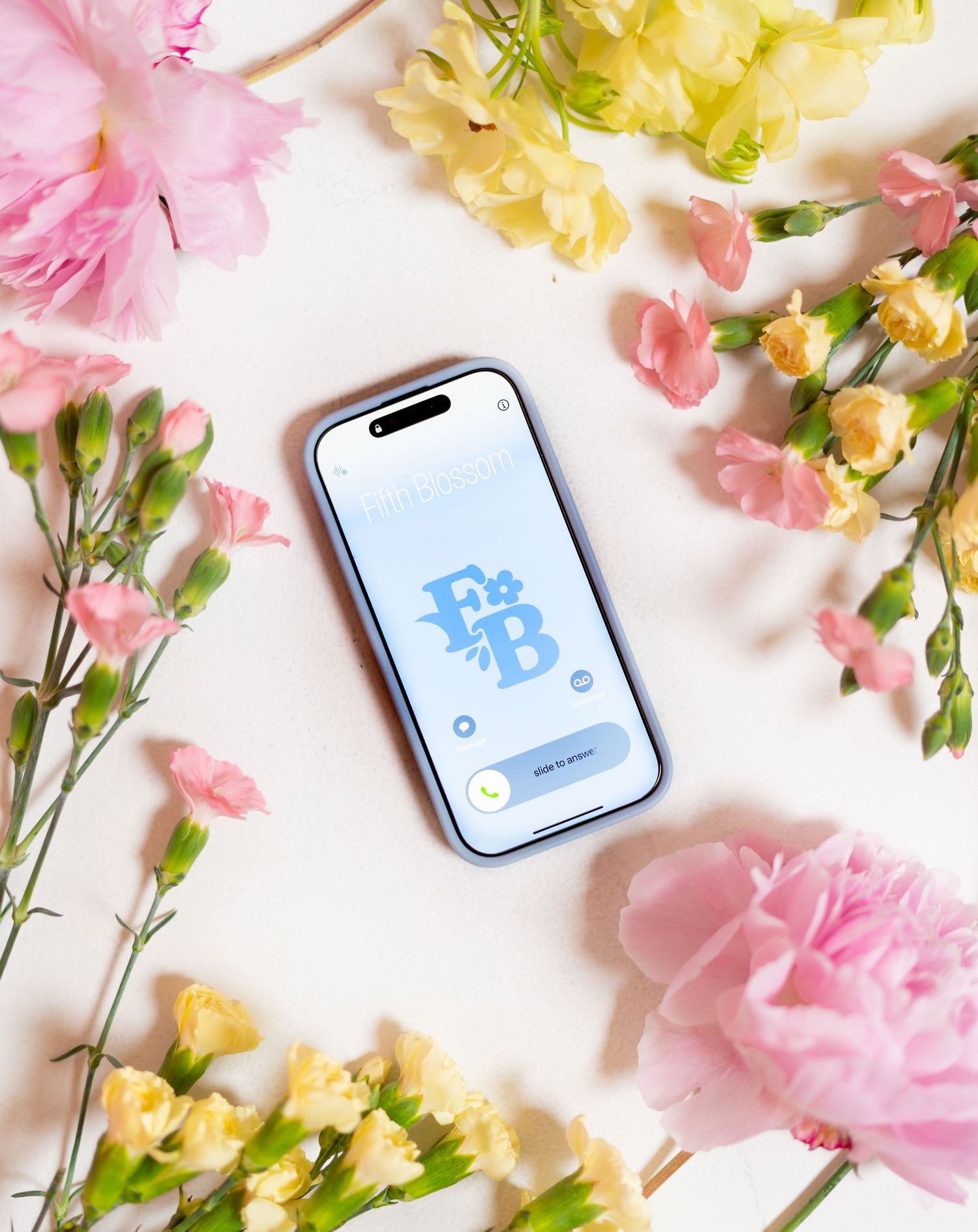 Floral flatlay with pink and yellow flowers surrounding a mobile phone on white background.