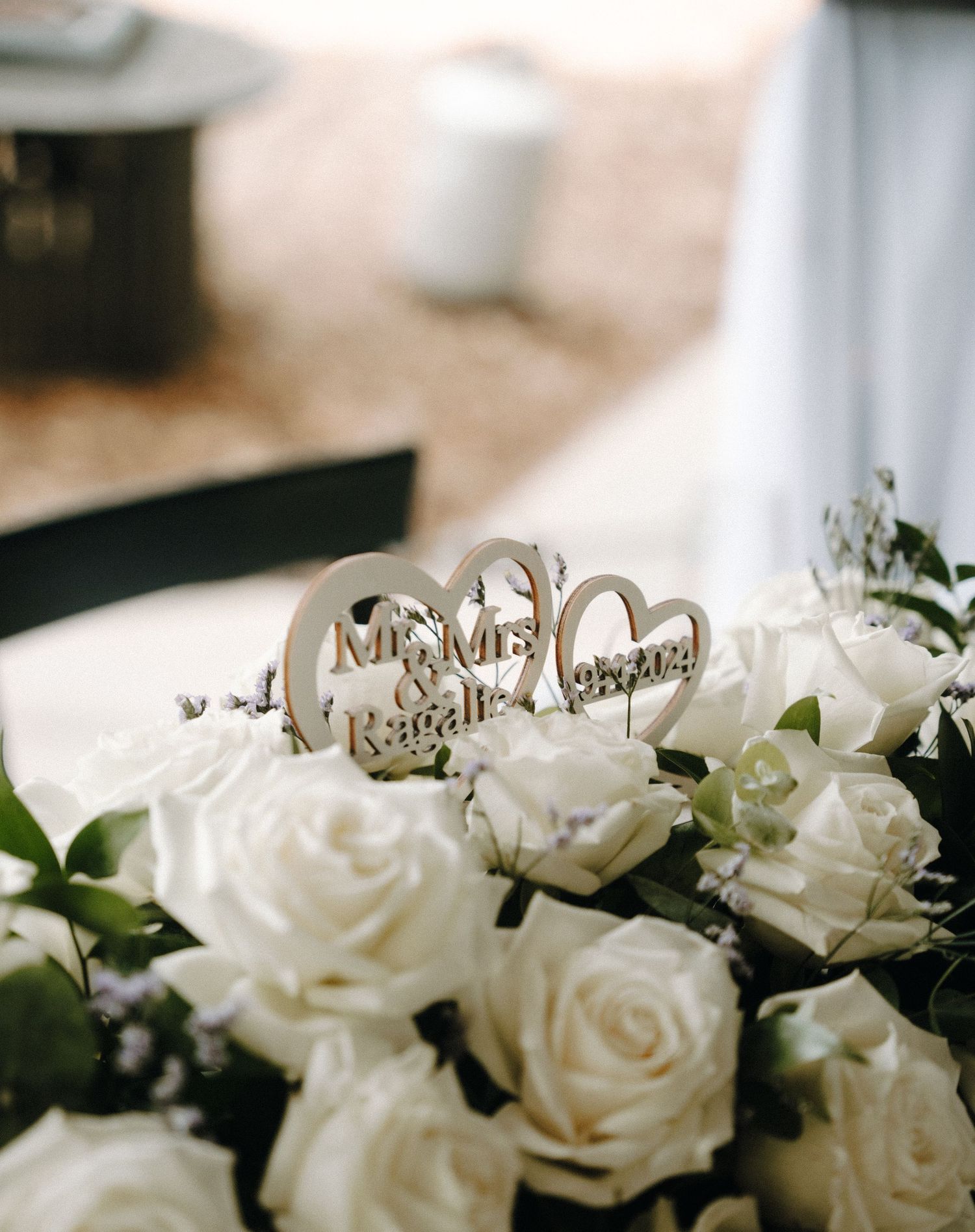 White roses and greenery arranged with wedding decorations on table.