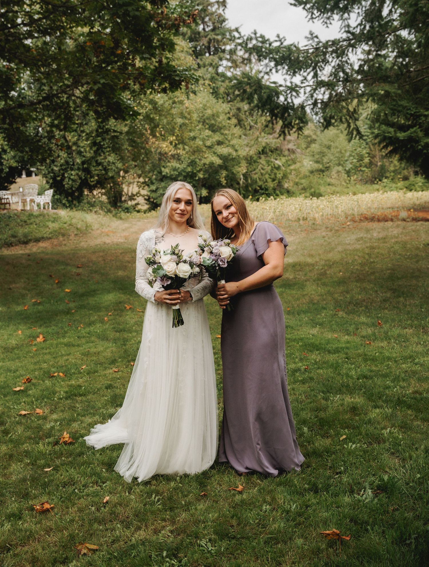 Wedding party in purple and white dresses standing together on grass.