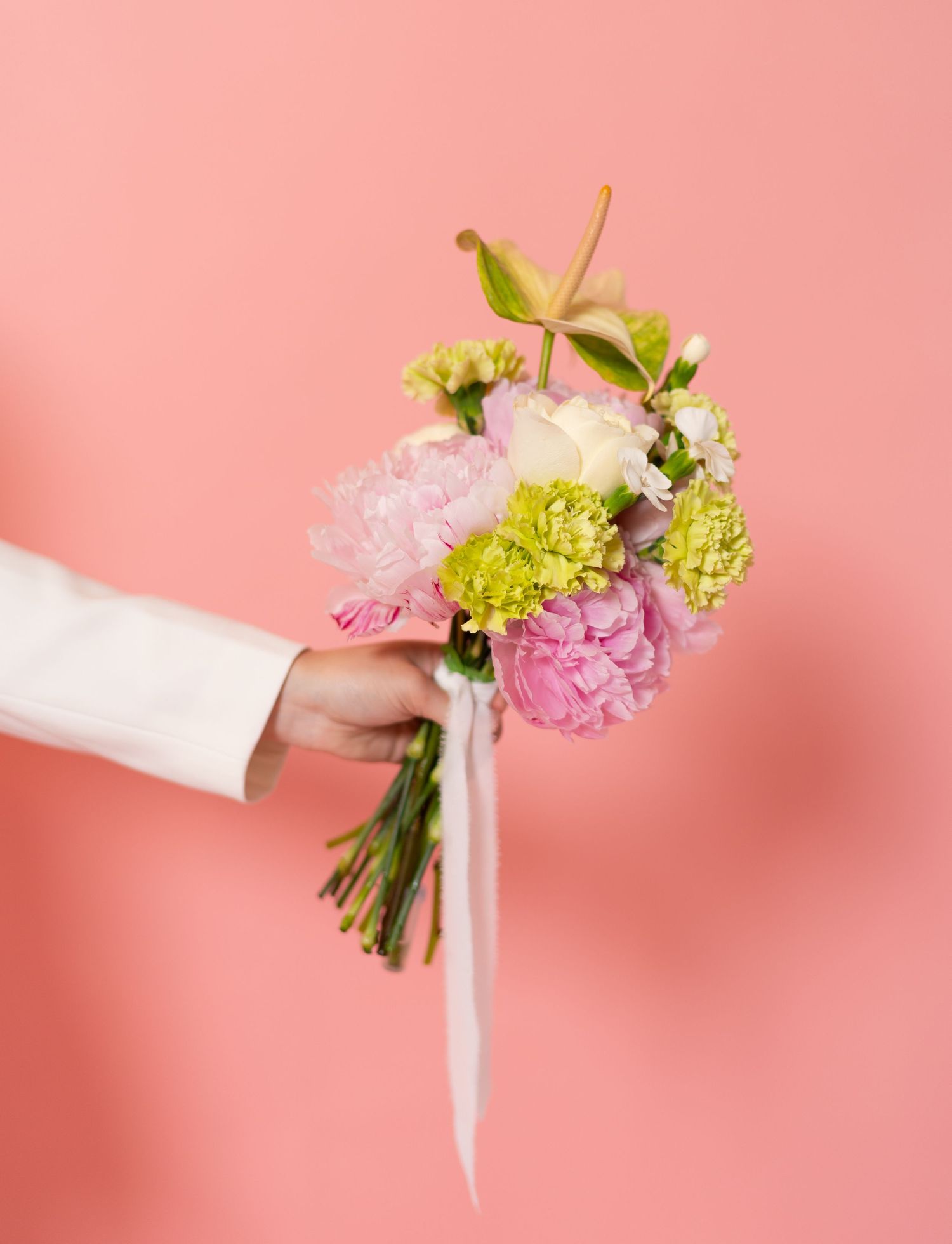 Hands holding fresh flower bouquet with pink and green blooms against coral background.
