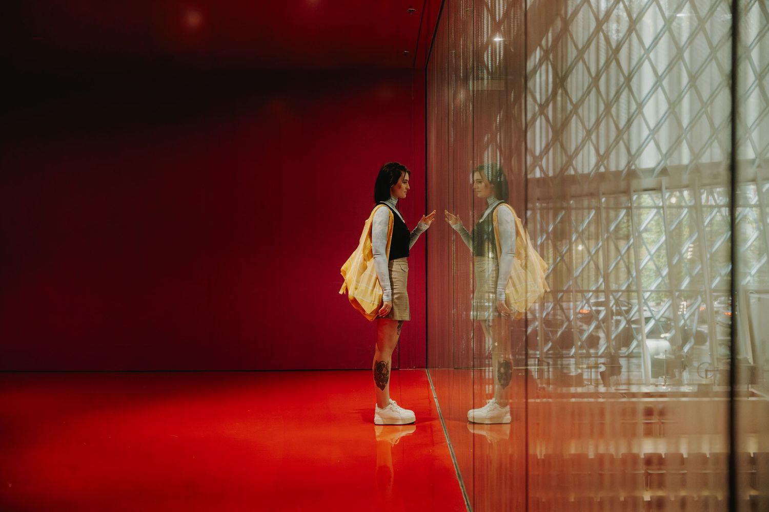 Silhouette shows a person in flowing yellow dress jumping gracefully against a red illuminated background with glass windows.