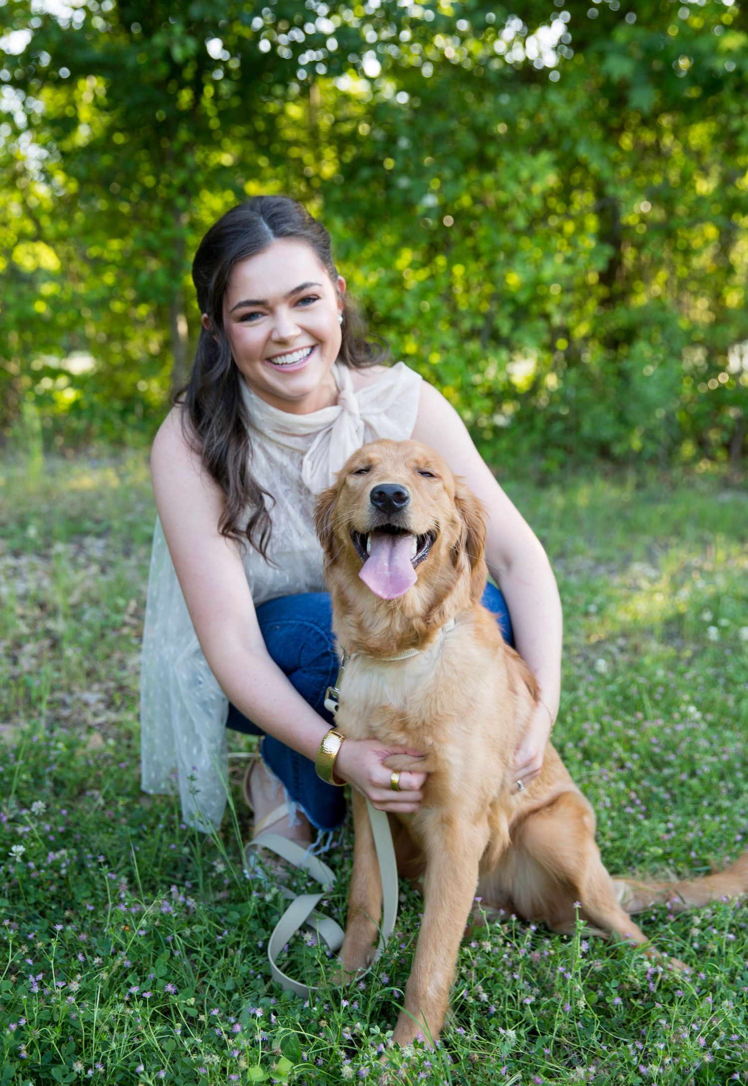 Happy golden retriever dog playing with woman in a sunny grassy area.