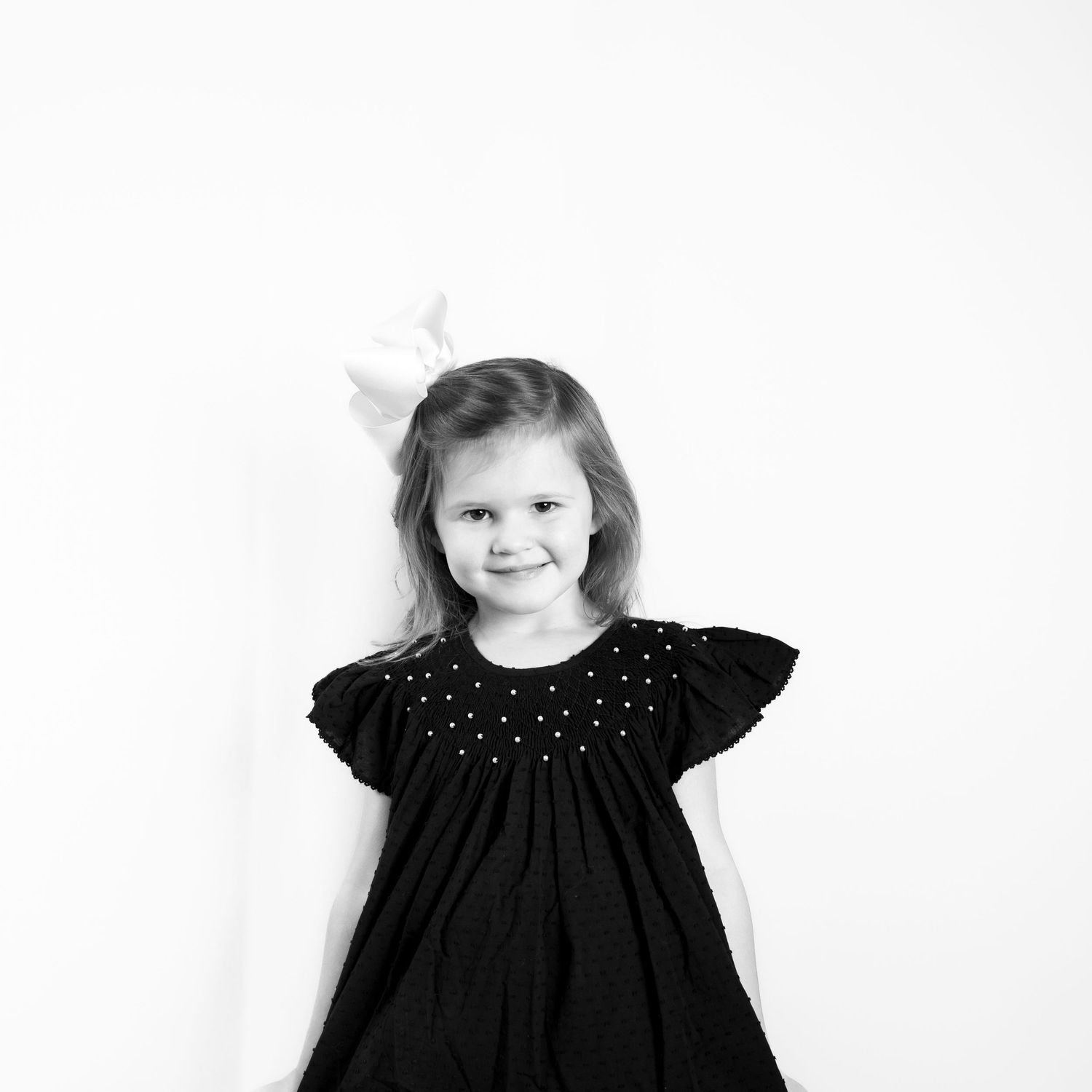 Three black and white portraits of a small child wearing a dark dress with polka dots against a light background.