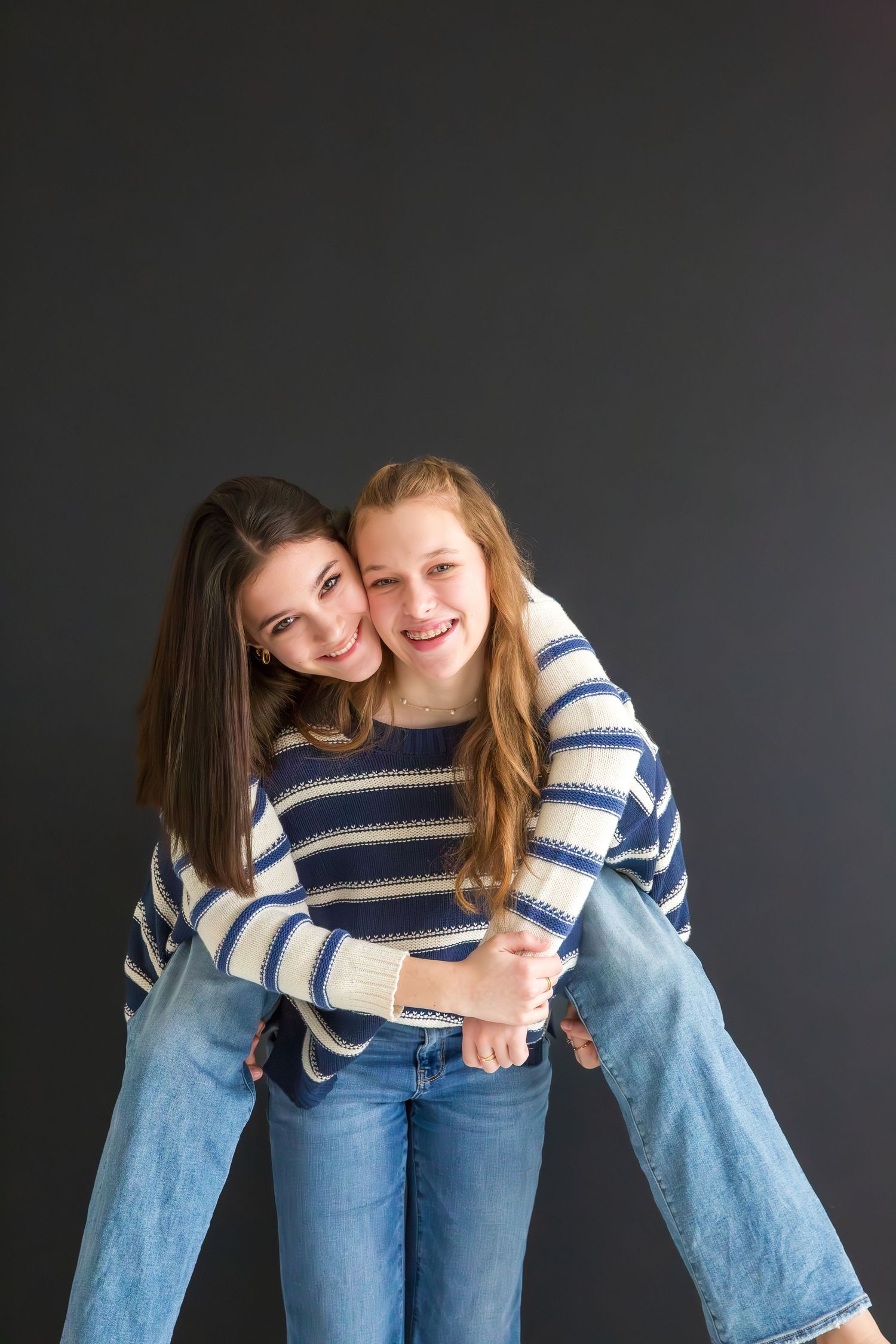 Two friends in striped sweaters and jeans embracing against dark background.
