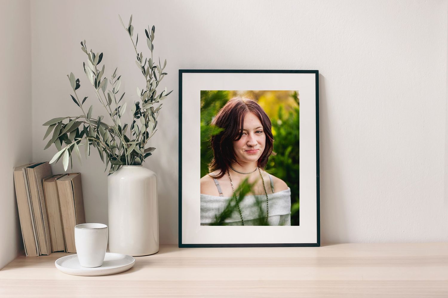 Minimalist wall display with framed teen headshot and greenery on light wooden shelf.