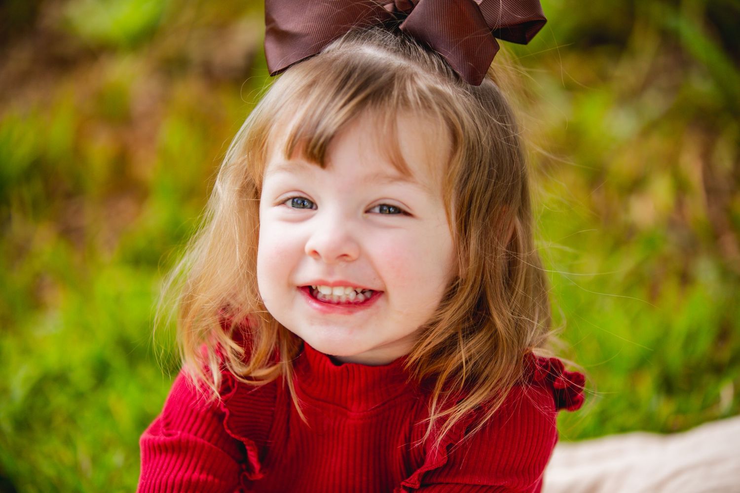 Child in red sweater smiling outdoors during autumn photo session.