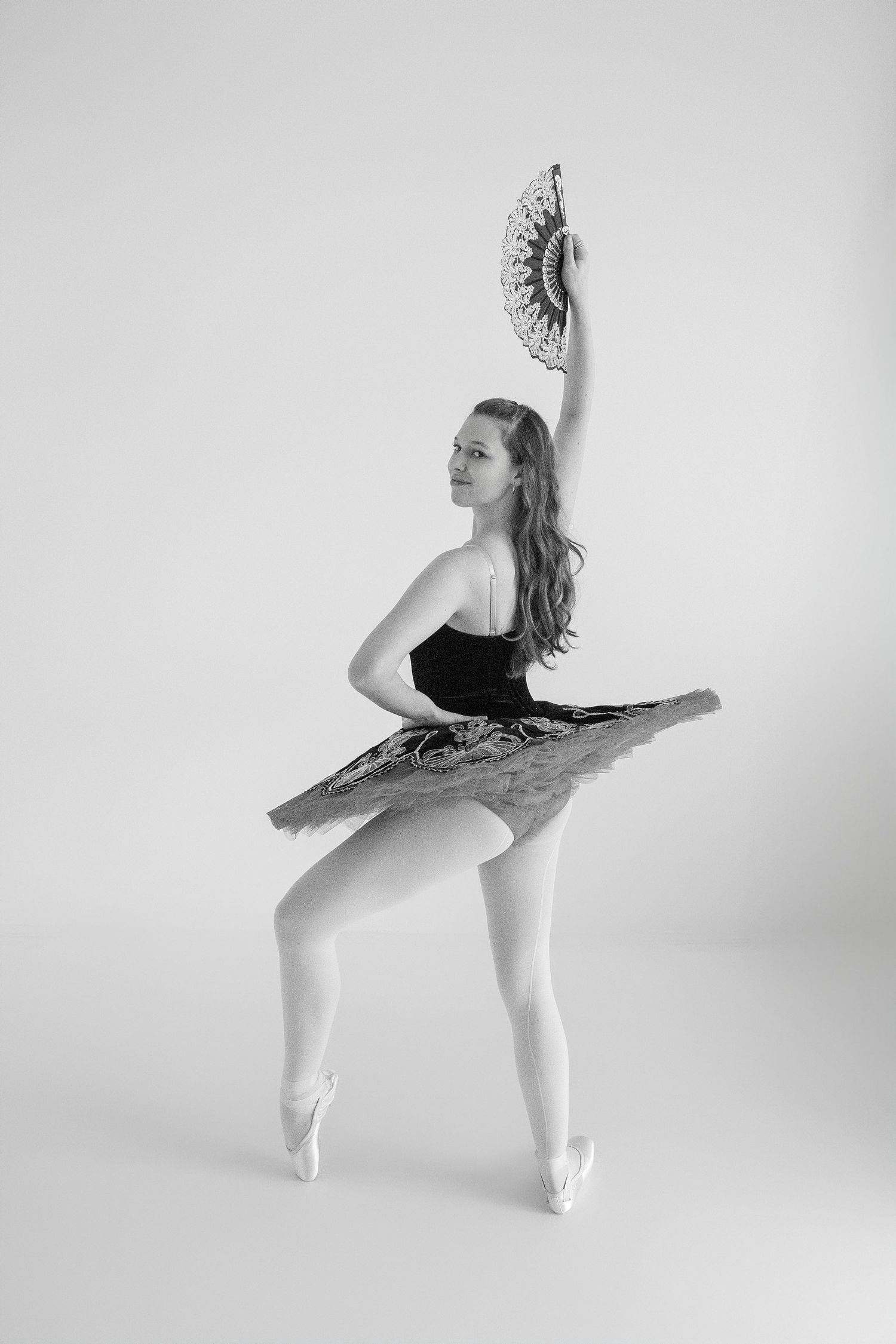 Ballet dancer in black leotard performing graceful poses in white studio setting.