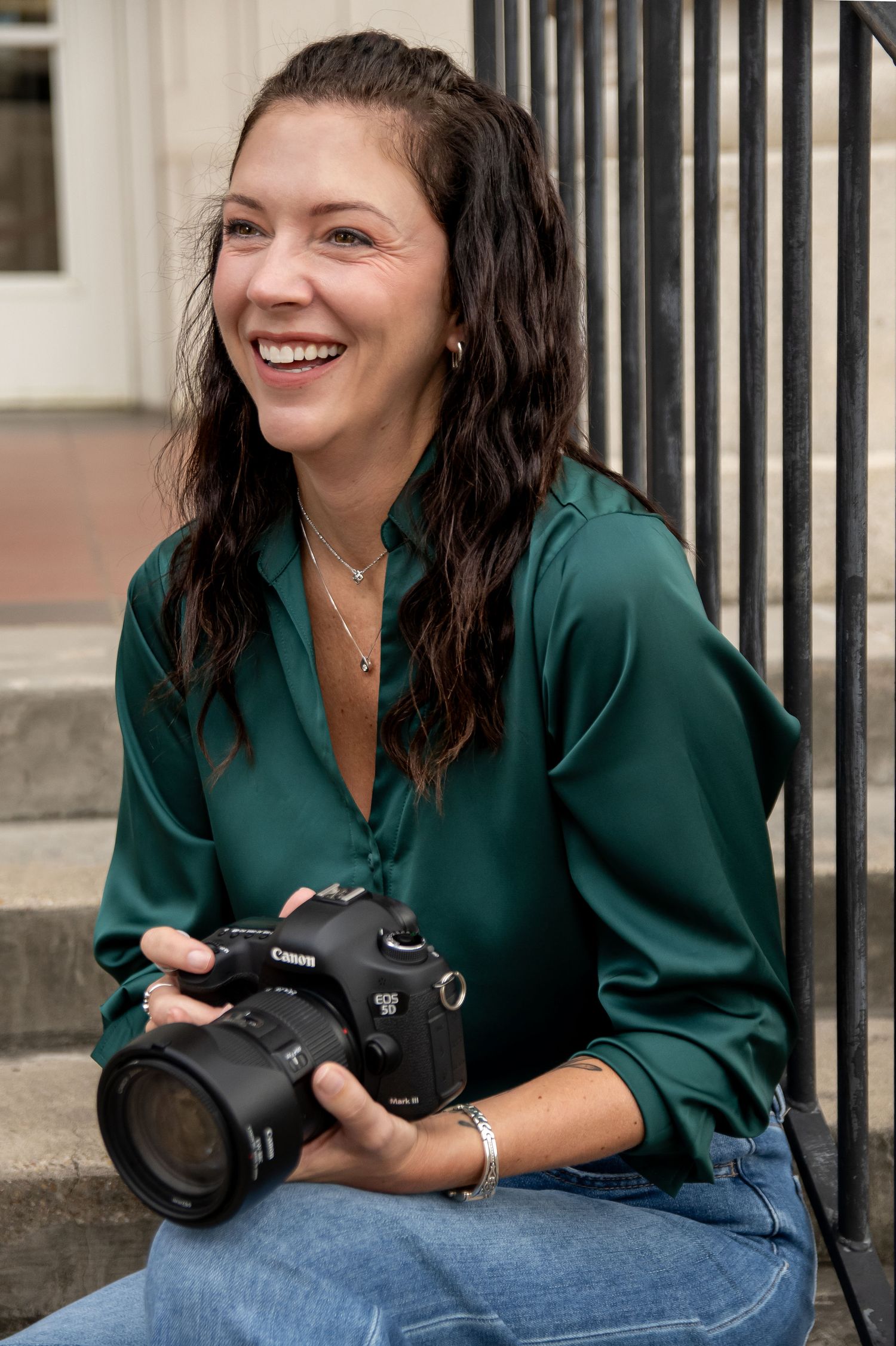 Photographer in dark green shirt holds camera while sitting on steps.