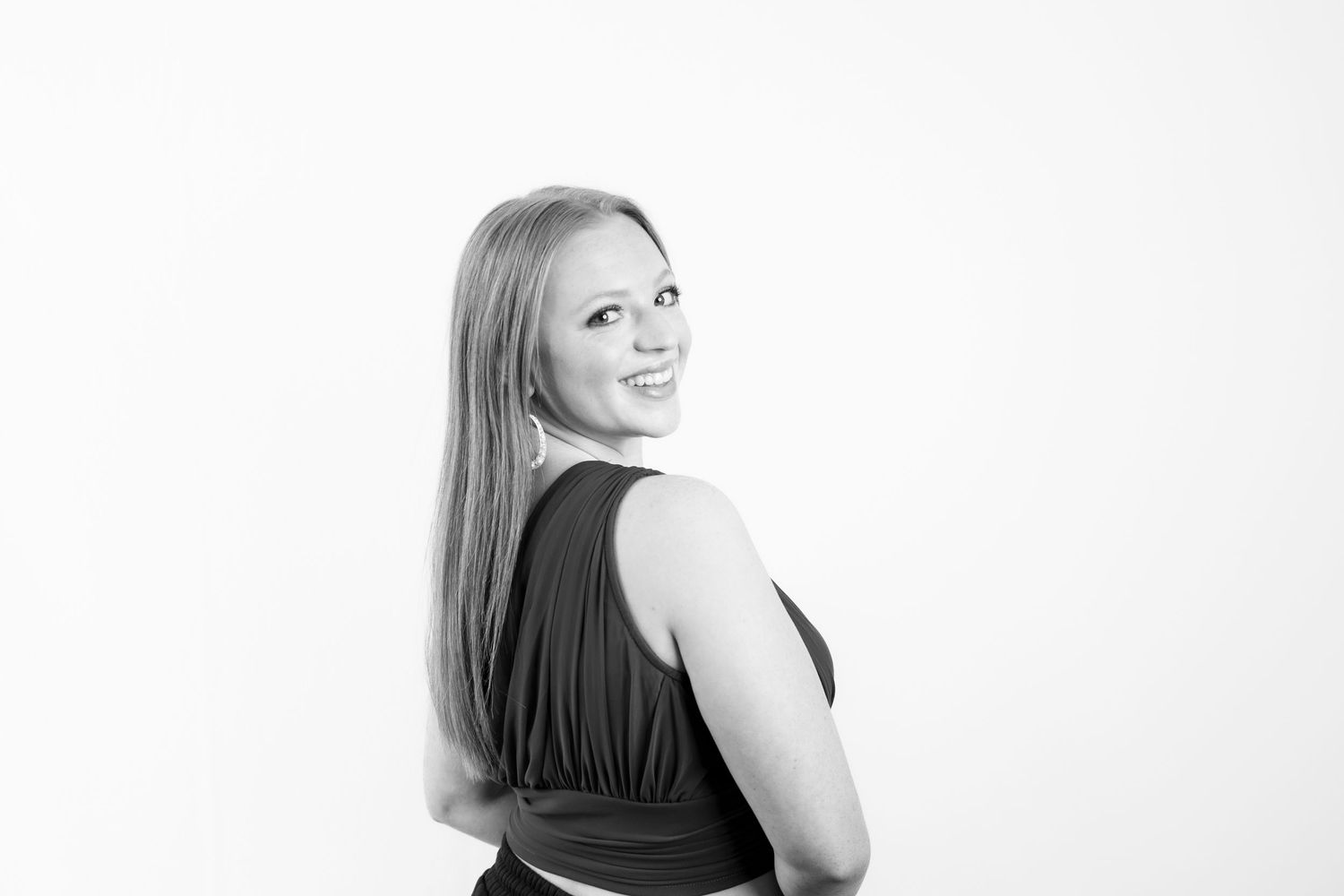 Black and white portrait of someone with long blonde hair looking over their shoulder and smiling against a white background.