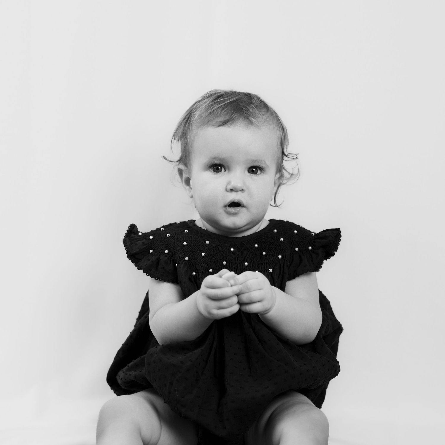 Black and white photo of a baby wearing a ruffled dress.
